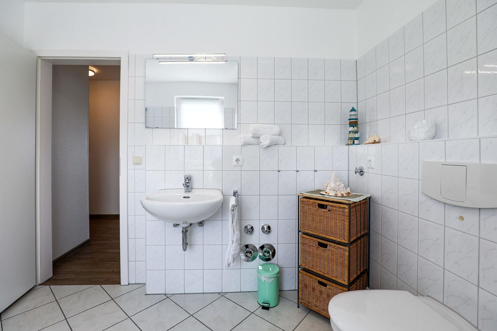 Bathroom with sink, mirror, toilet, and wicker storage unit.