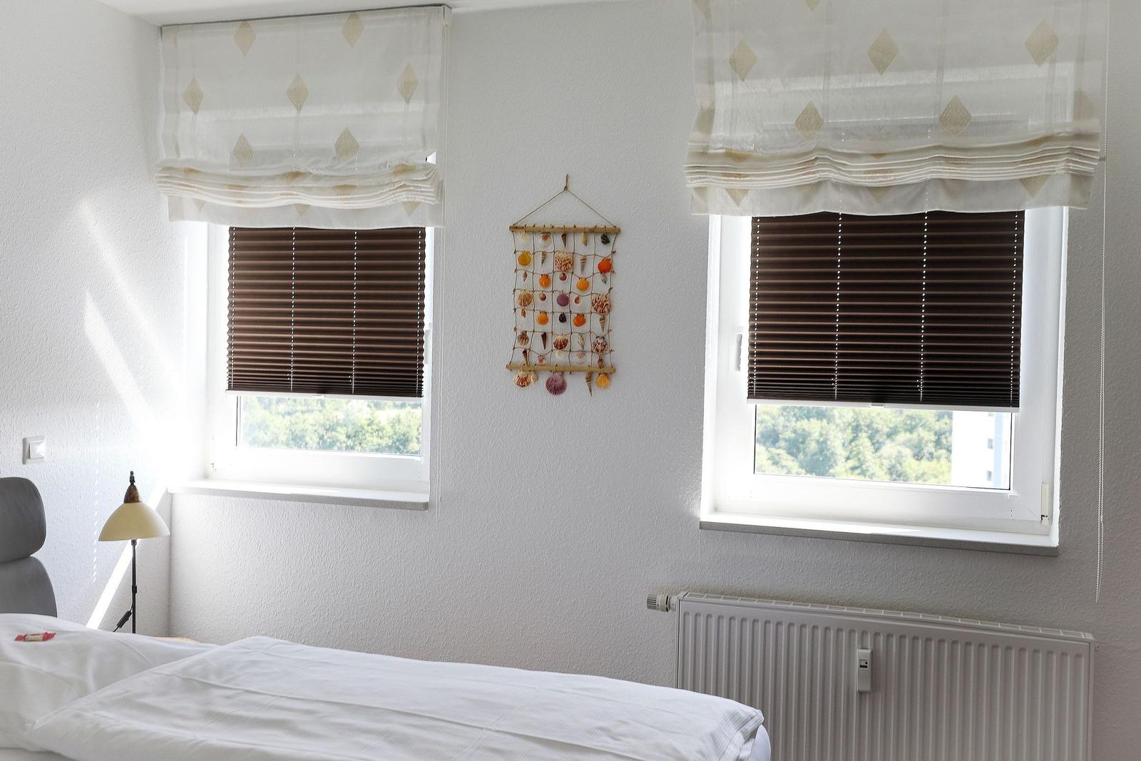 Room with bed, two windows, and wall lamp. Wall decoration with seashells.