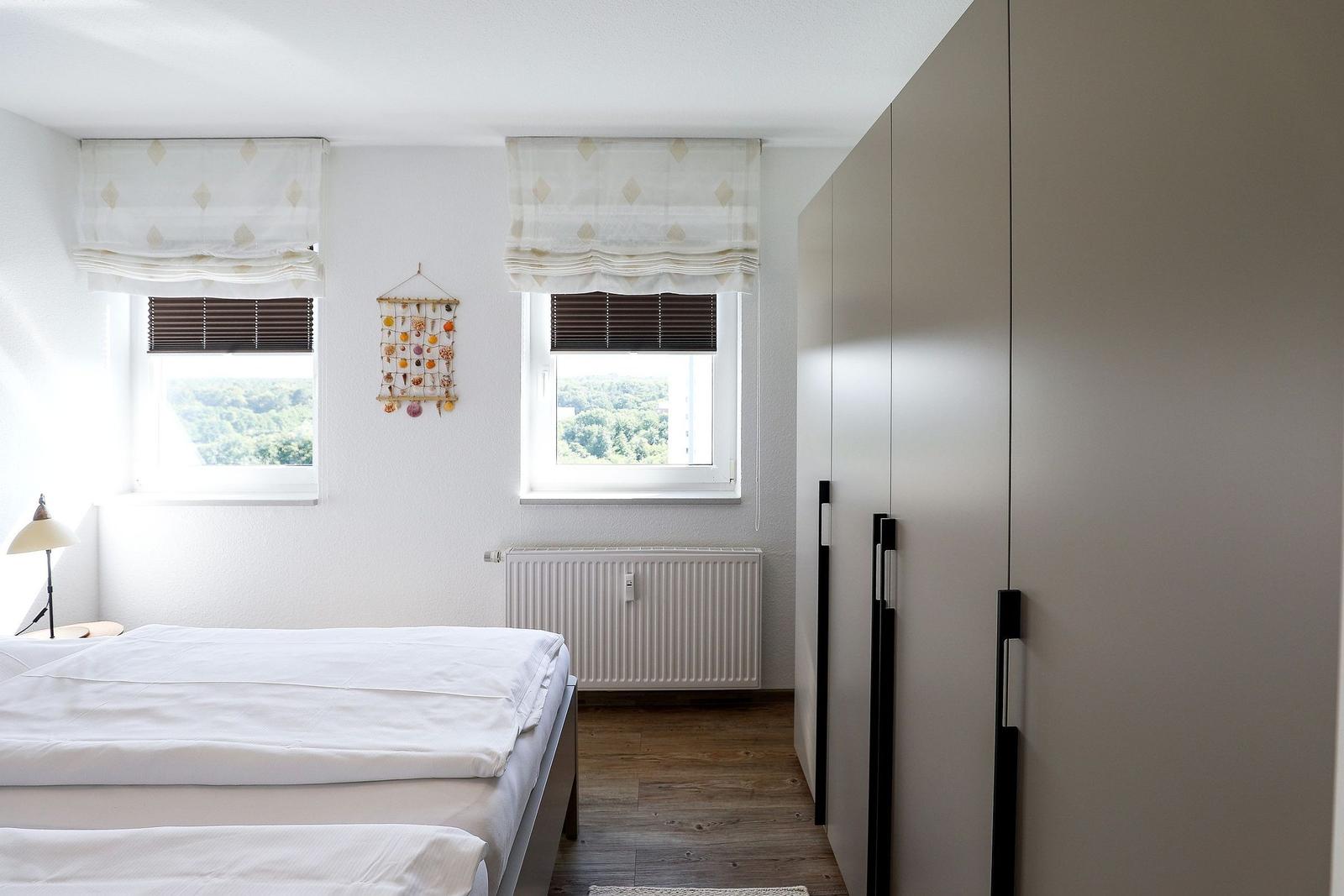 Bedroom with double bed, two windows, and wardrobe. View of green landscape.