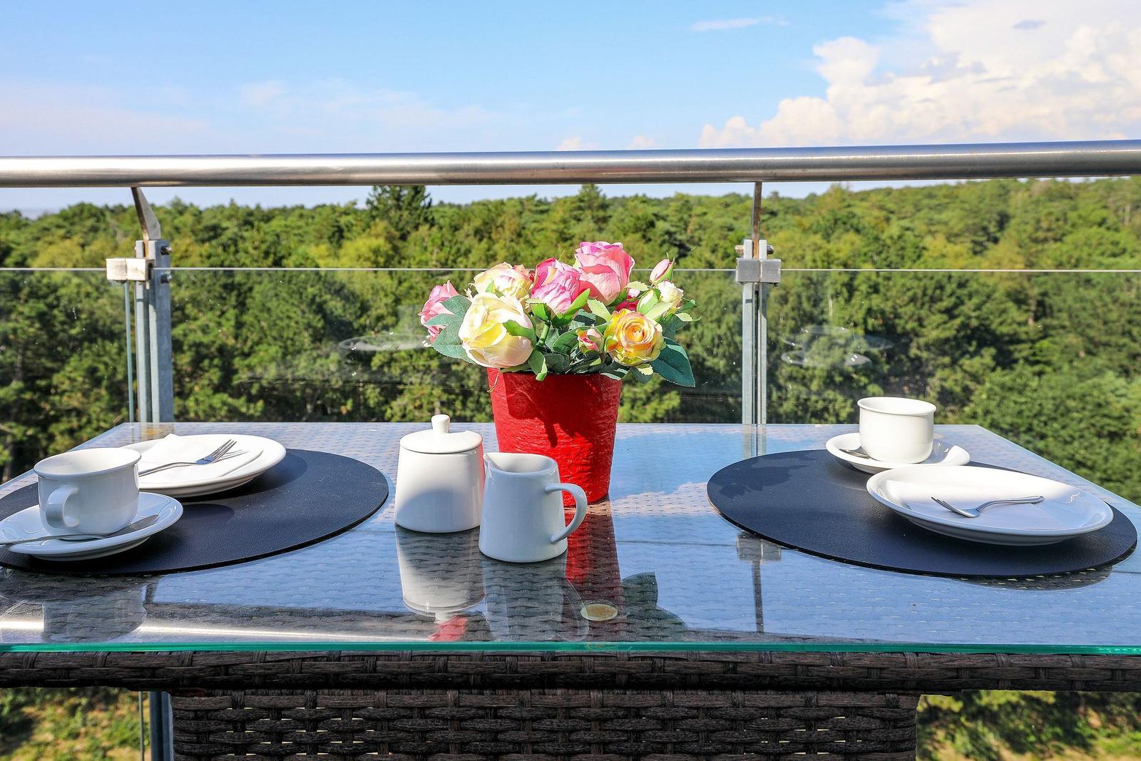 Terrace with table, two places, flowers, and view of forest.