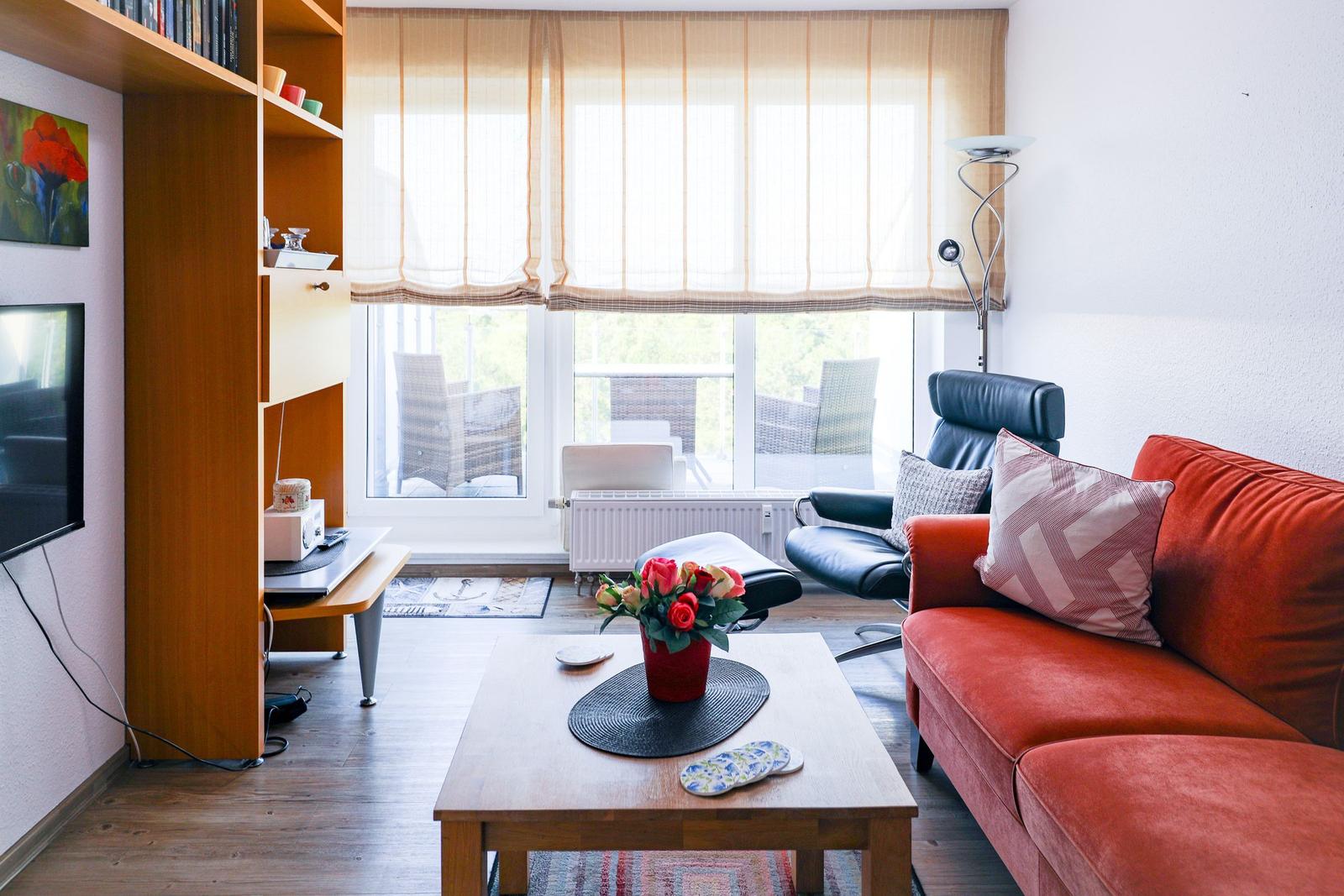 Living room with red sofa, wooden table, and view of balcony.