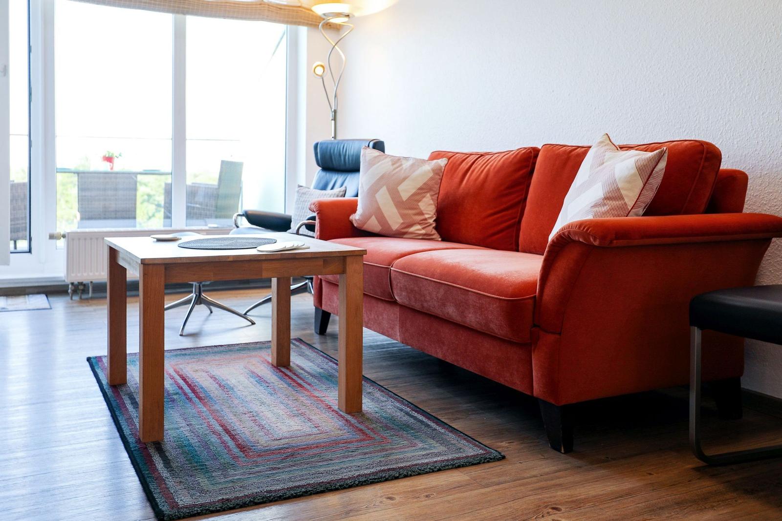A living room with an orange sofa, wooden table, and colorful rug.