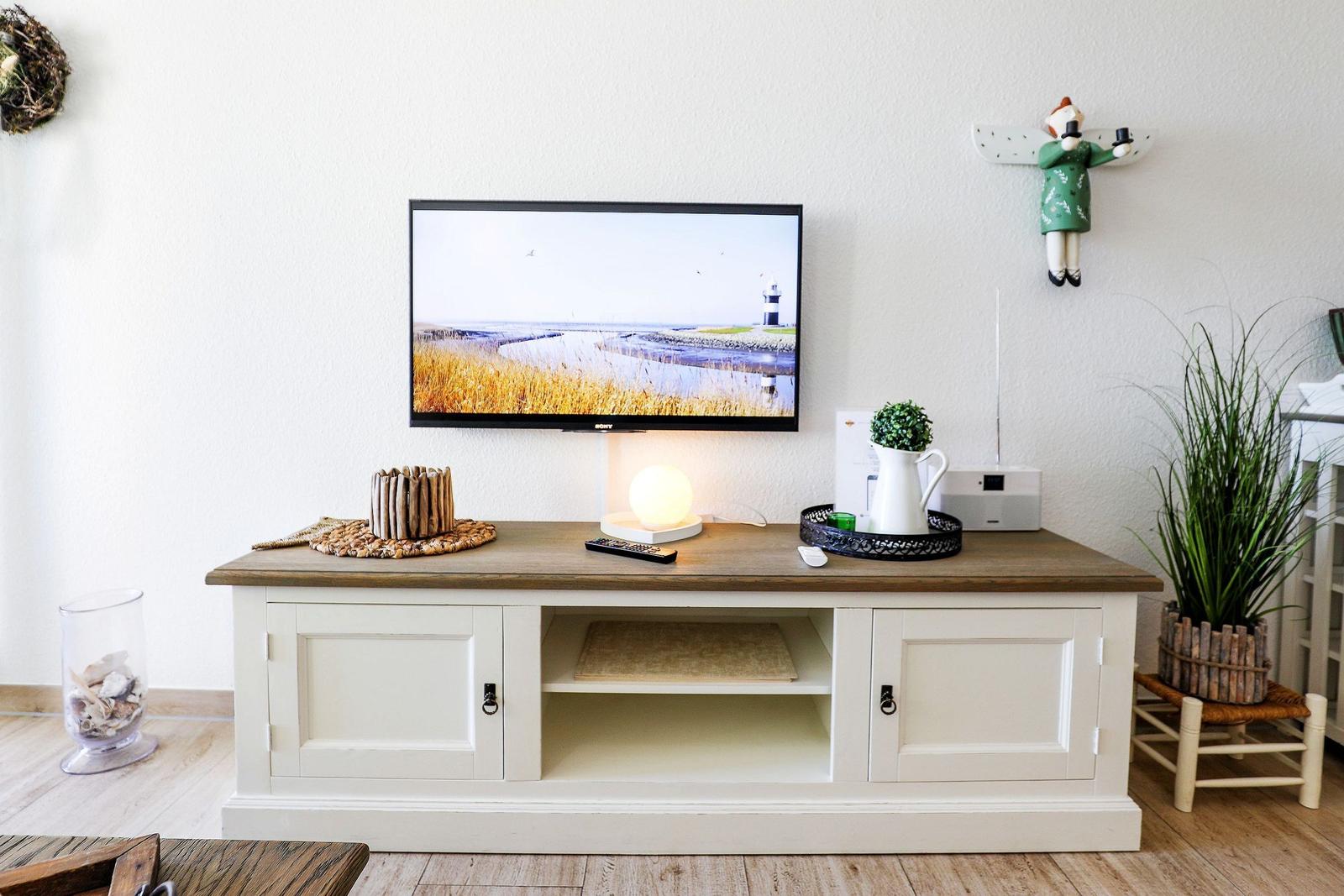 TV auf Holzkonsole mit Lampe, Pflanzen und Dekoration.