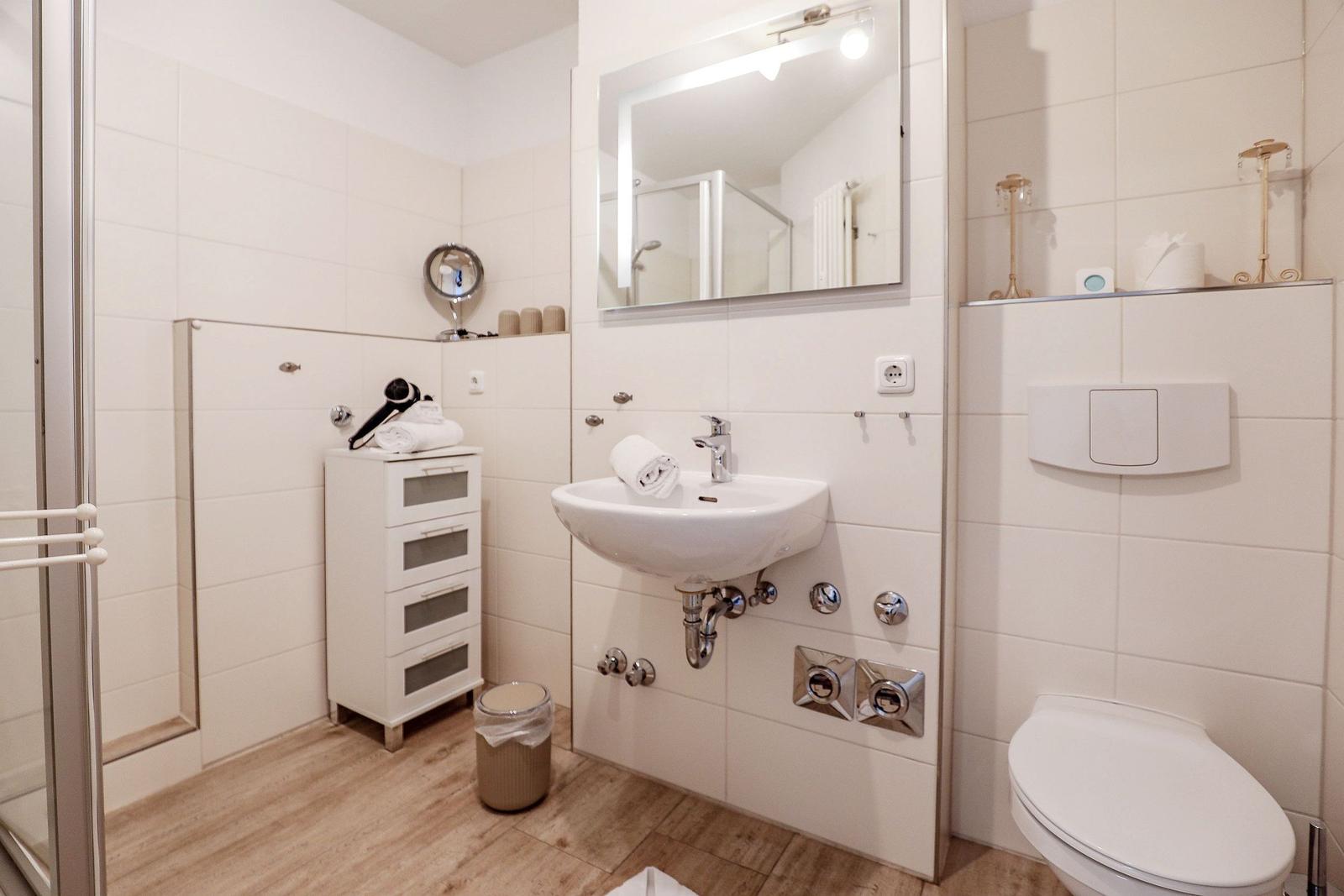 Badezimmer mit Waschbecken, Spiegel, Toilette und Dusche.