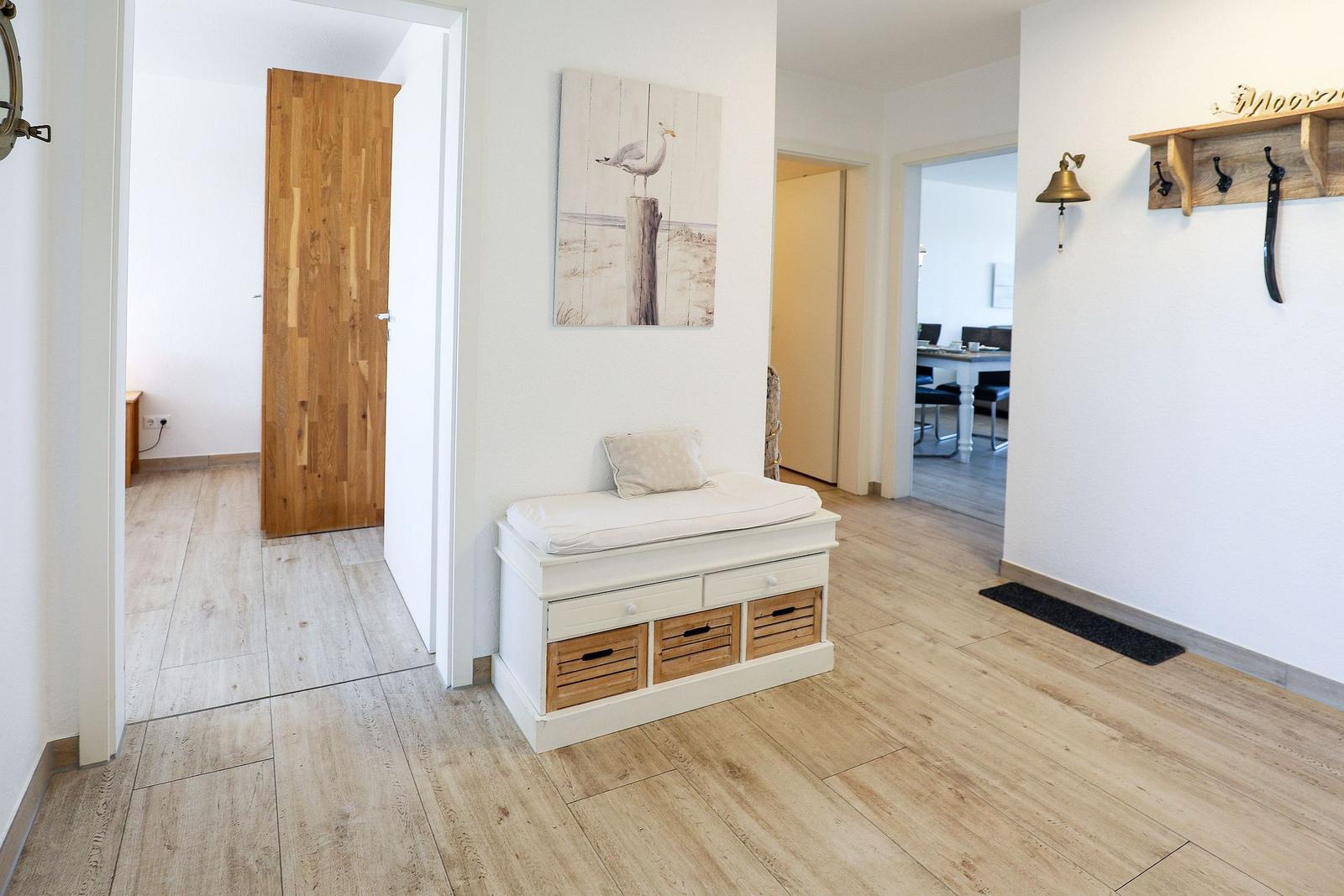 Eingangsbereich mit Sitzbank, Wandbild und Hakenregal. Holzboden und weiße Wände.