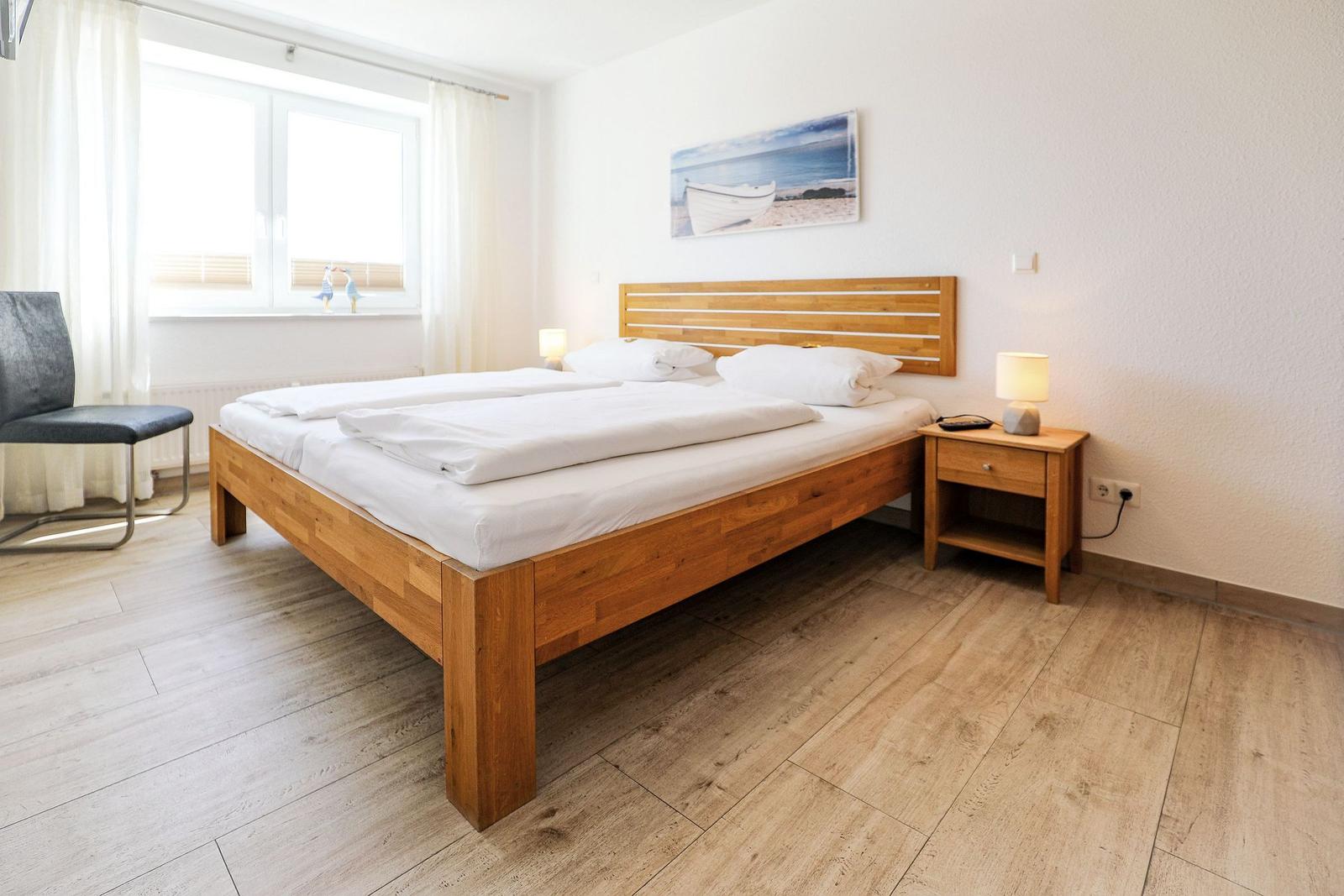 Schlafzimmer mit Holzbett, Nachttisch und Fenster. Wandbild zeigt Boot.