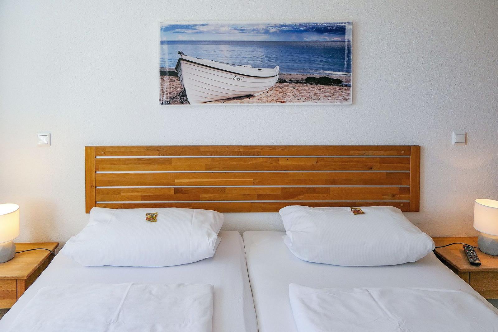 Doppelbett mit Holz-Kopfteil, zwei Nachttische und Wandbild mit Boot.