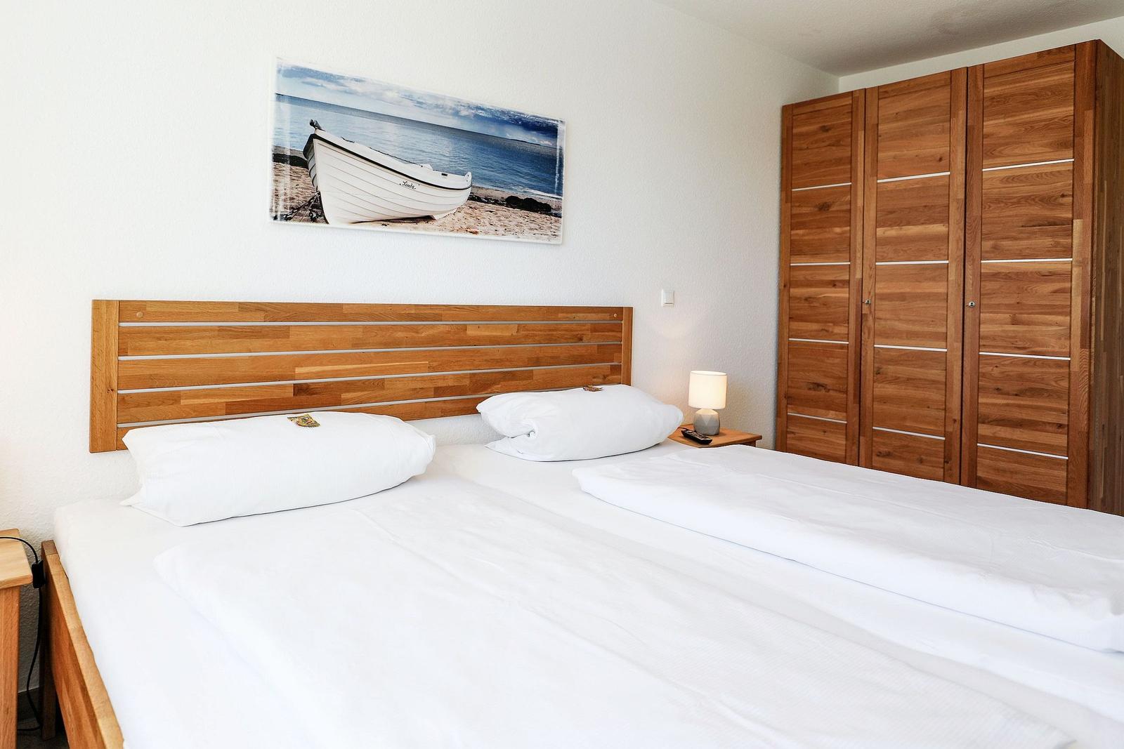 Schlafzimmer mit Doppelbett, Holzschrank und Wandbild mit Boot.