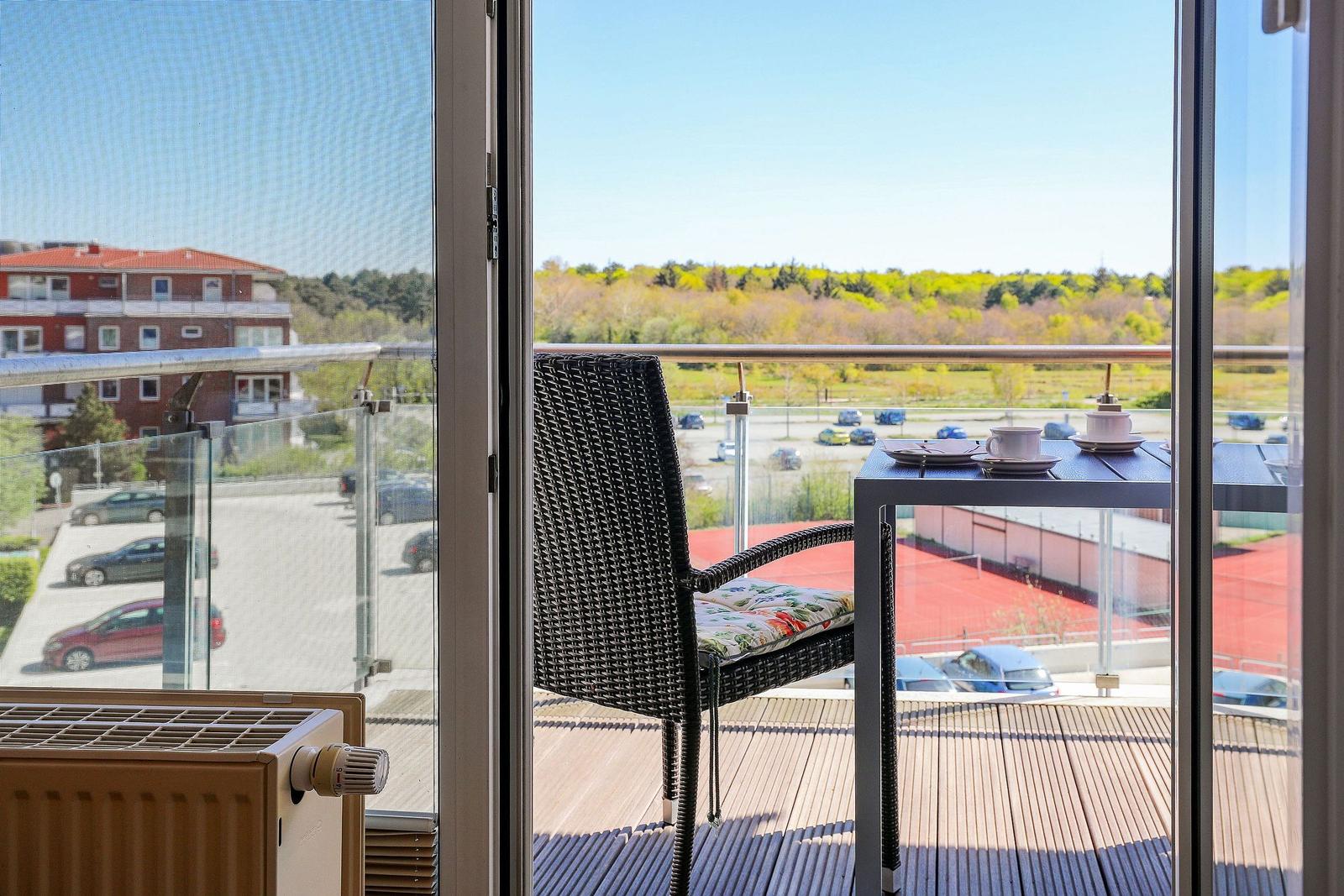 Balkon mit Stuhl und Tisch, Blick auf Parkplatz und Wald.