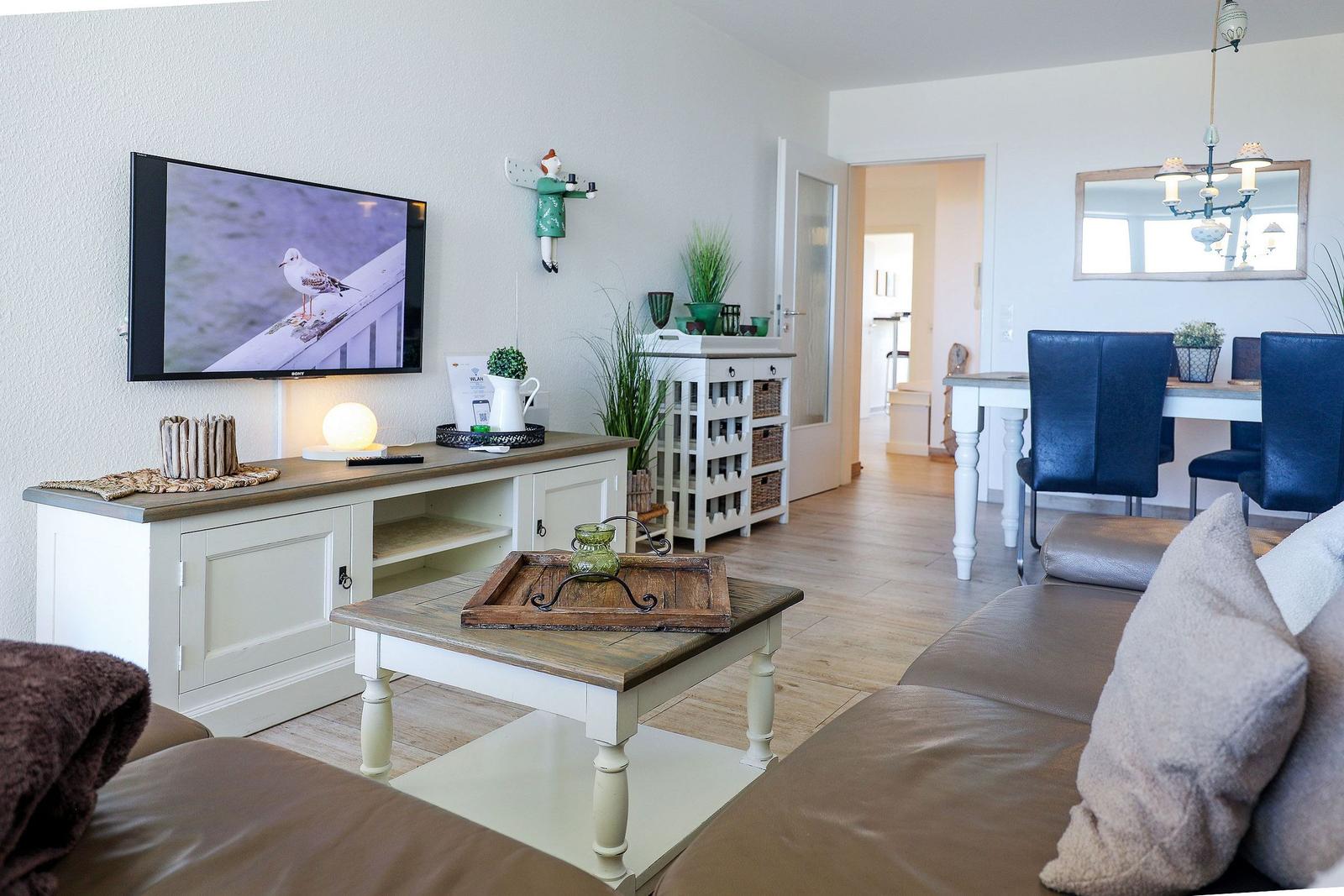 Wohn- und Essbereich mit Sofa, TV, Esstisch und Küchenbereich im Hintergrund.