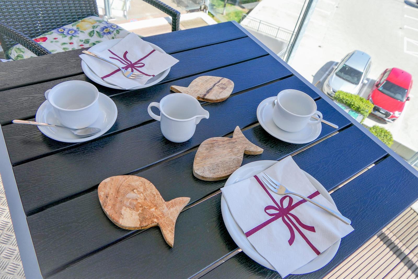 Tisch mit Tassen, Tellern und Fischformen aus Holz auf Balkon.
