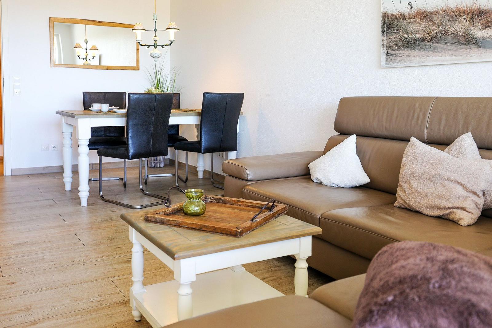 Wohn- und Essbereich mit braunem Sofa, weißem Tisch und schwarzen Stühlen.