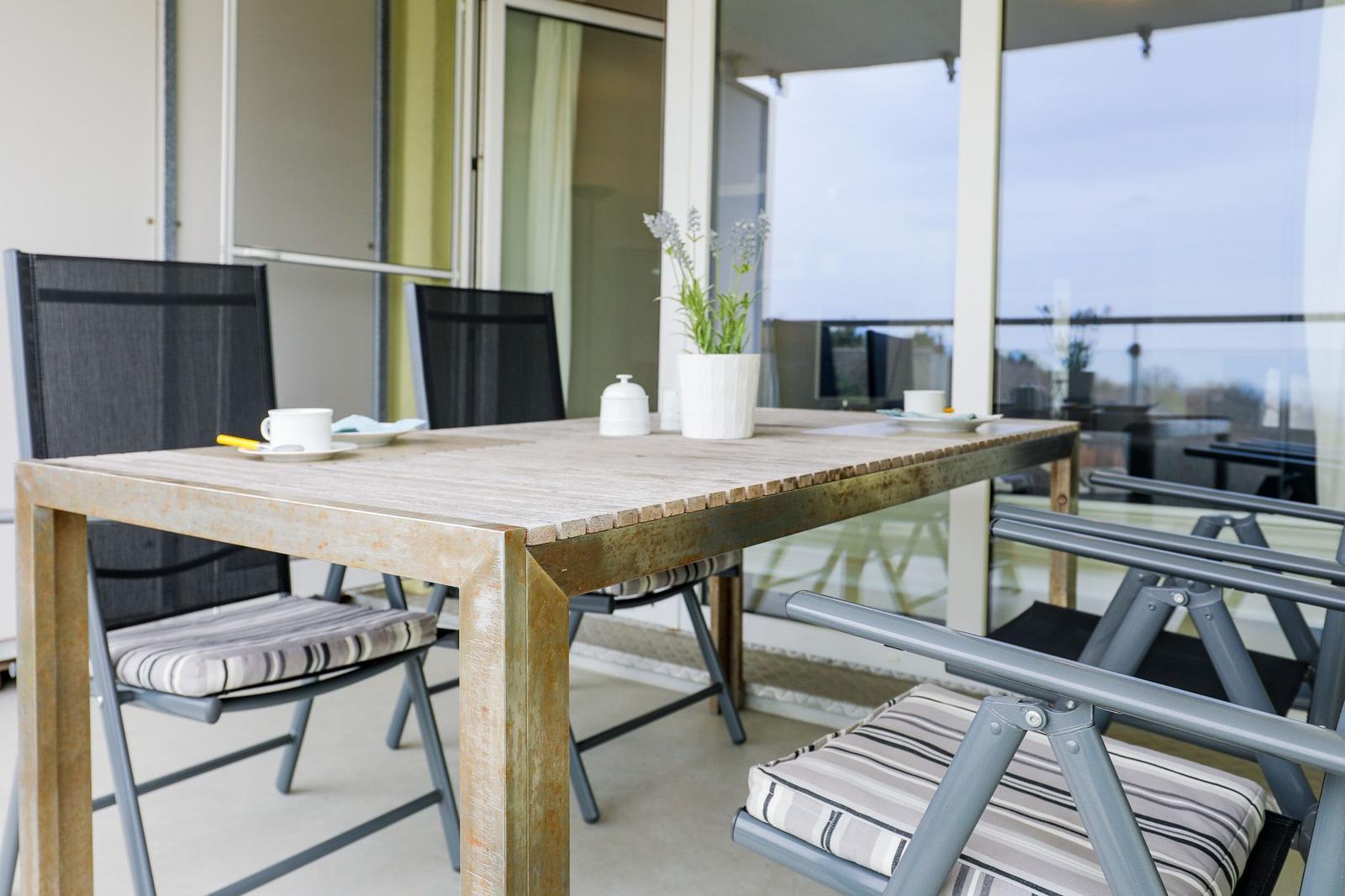 Terrasse mit Holztisch und Stühlen, Pflanze und Tasse.