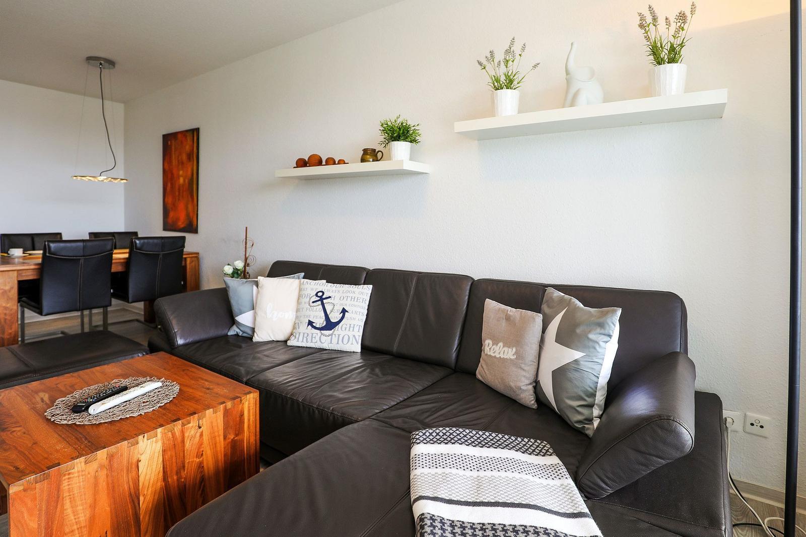 Schwarzes Sofa mit Kissen, Holztisch und Regale mit Pflanzen an der Wand.