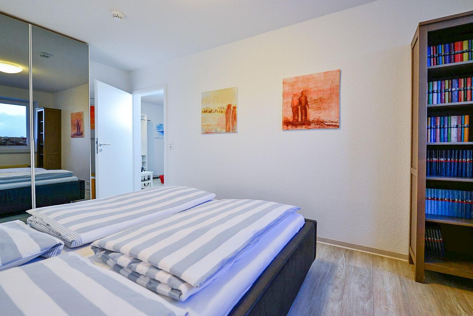 Schlafzimmer mit Bett, Bücherregal und Wandbildern.