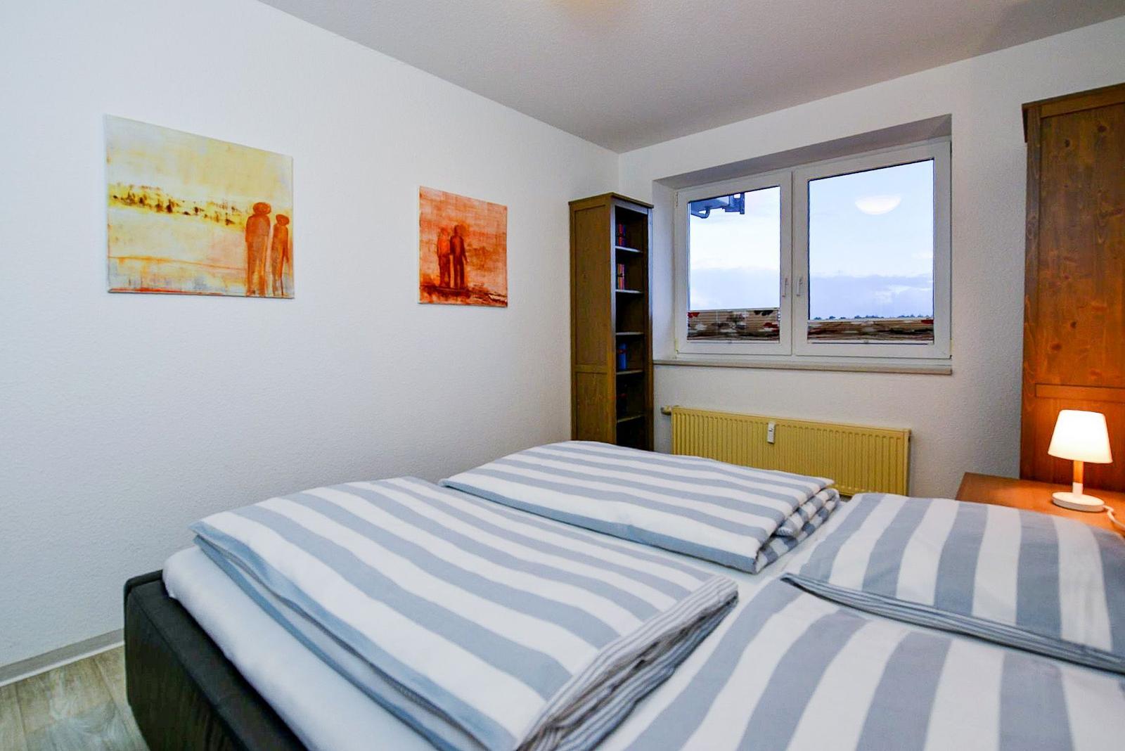 Zwei Betten mit gestreiften Bettwäsche, Wandbilder und Fenster mit Blick.
