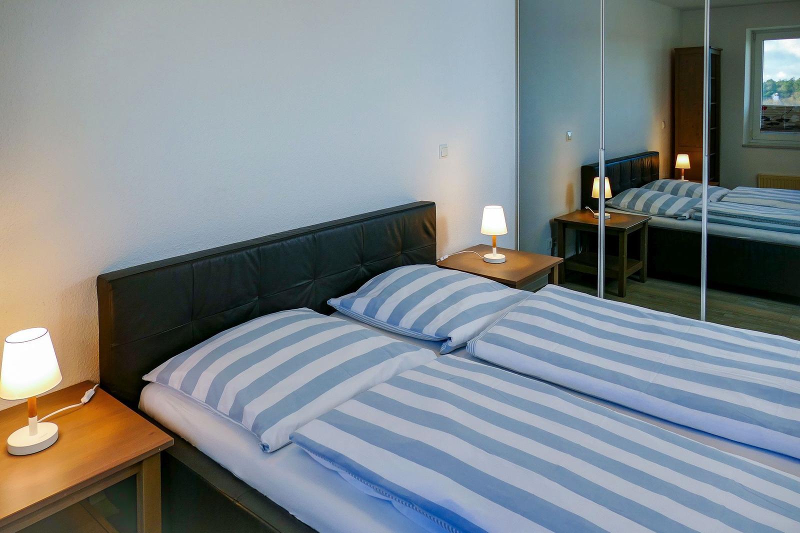 Schlafzimmer mit Doppelbett, zwei Nachttischen und Lampen. Spiegel reflektiert das Bett.