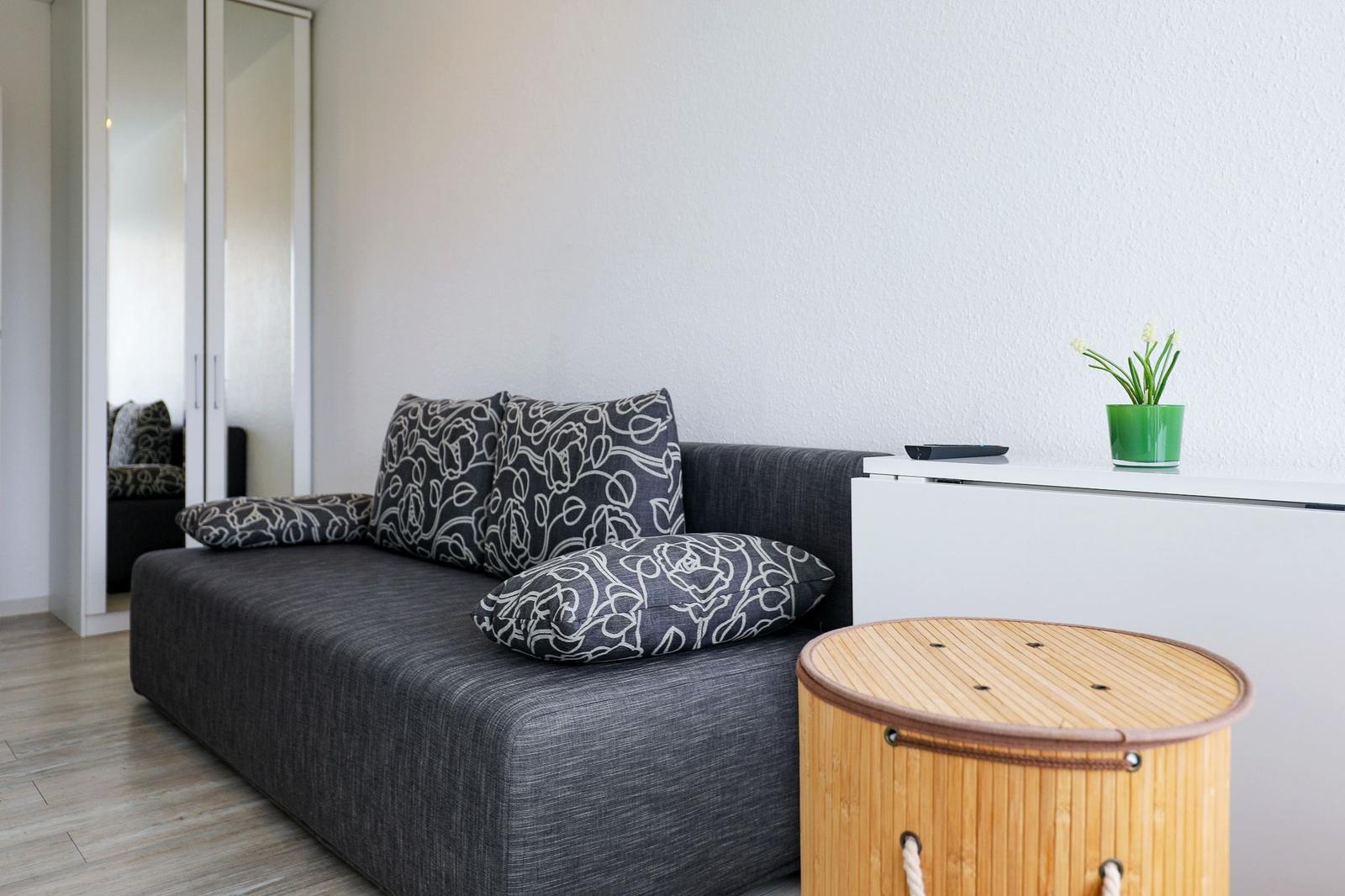 Ein grauer Sofa mit Mustermustern, ein runder Tisch und eine weiße Kommode.