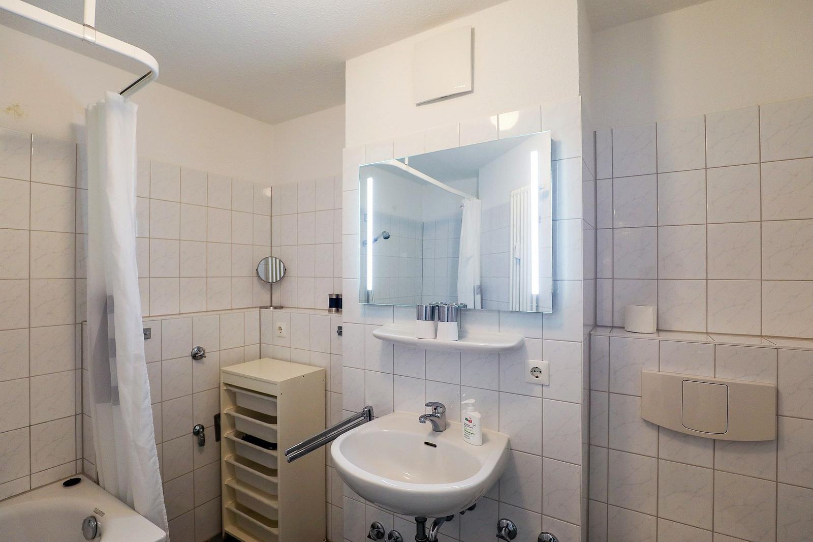 Badezimmer mit Dusche, Waschbecken und Spiegel. Fliesenwand und weiße Einrichtung.