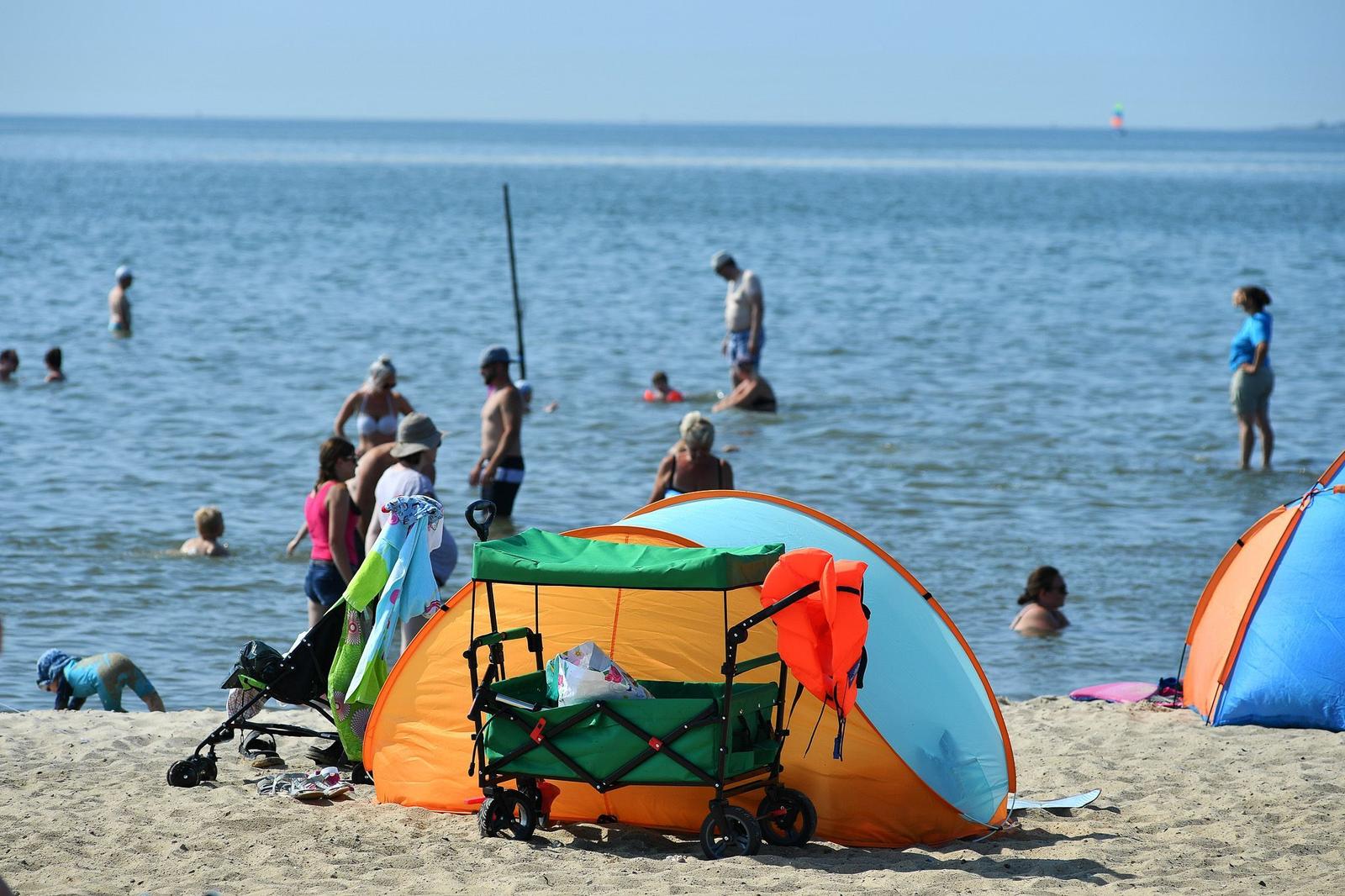 Strand mit bunten Zelten und Menschen im Wasser.