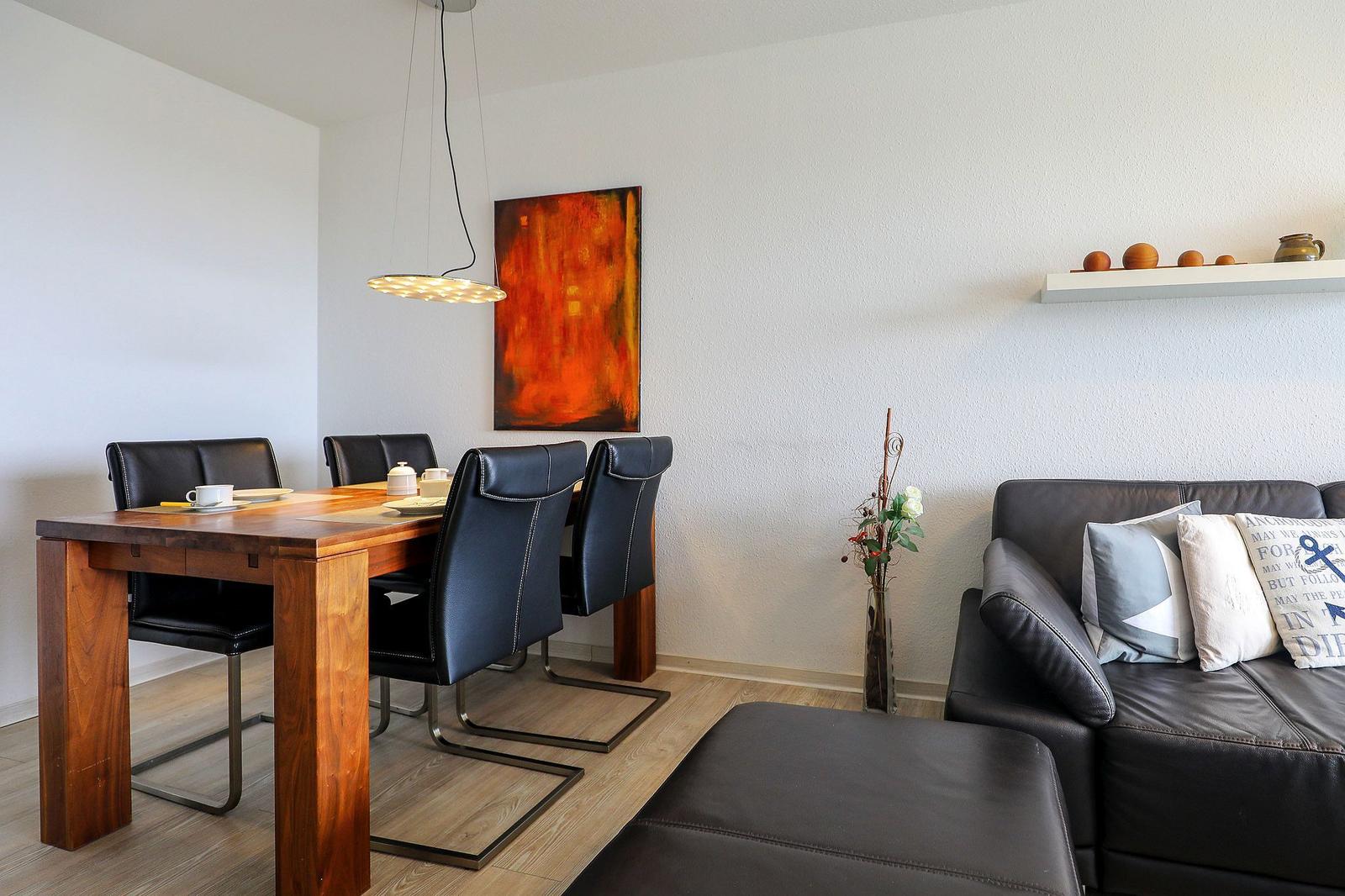 Essbereich mit Holztisch und schwarzen Stühlen. Wohnbereich mit Ledersofa und Kissen.