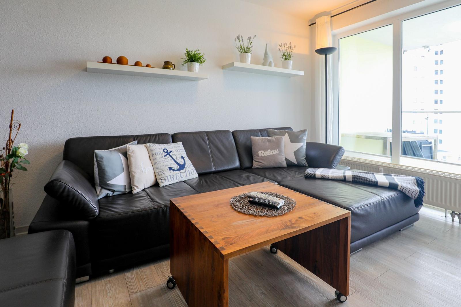 Schwarzes Ledersofa mit Kissen, Holztisch und Fenster mit Blick.