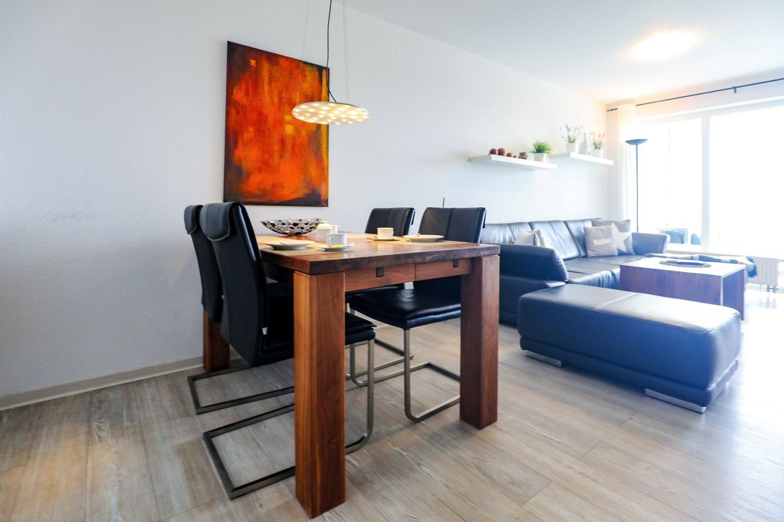 Essbereich mit Holztisch und schwarzen Stühlen. Wohnbereich mit Sofa und Ottomane.