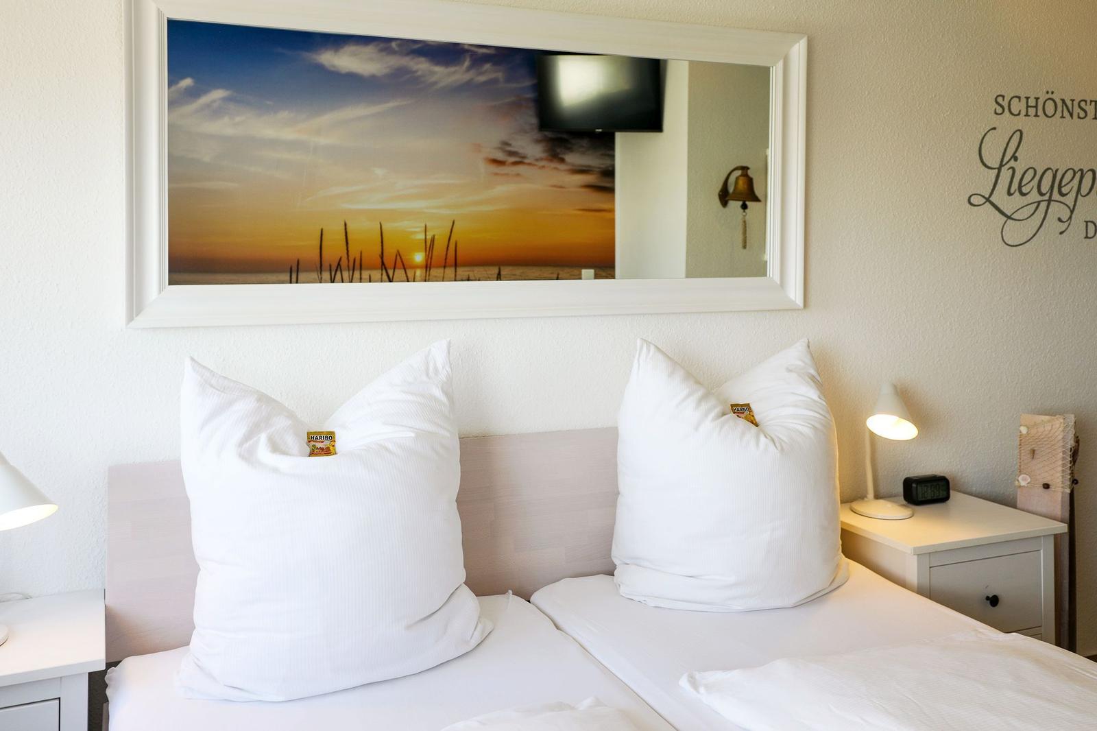 Zwei Betten mit weißen Kissen und Kopfkissen. Über dem Bett hängt ein Bild mit Sonnenuntergang.