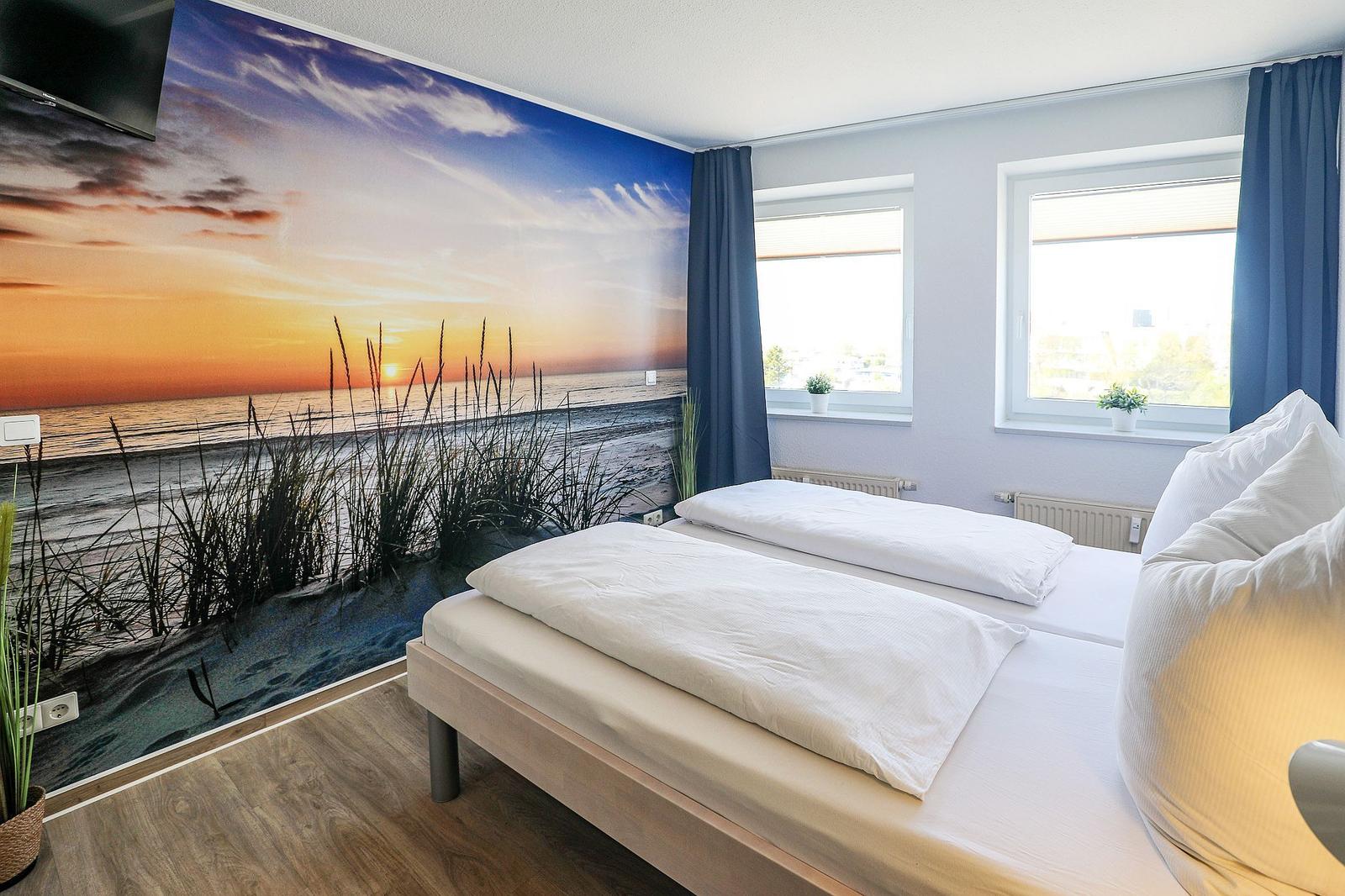 Zimmer mit Bett, Wandbild und Fenstern.
