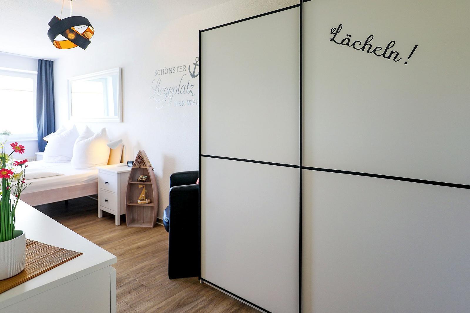 Schlafzimmer mit Bett, Nachttisch und Schwebetüren. Wanddekoration und Blumen sichtbar.