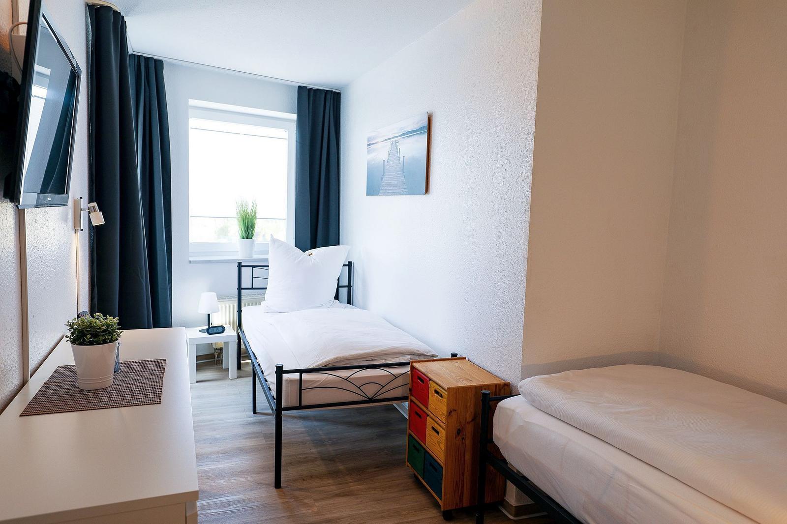 Zwei Einzelbetten, Schreibtisch, TV und Fenster mit Vorhängen.