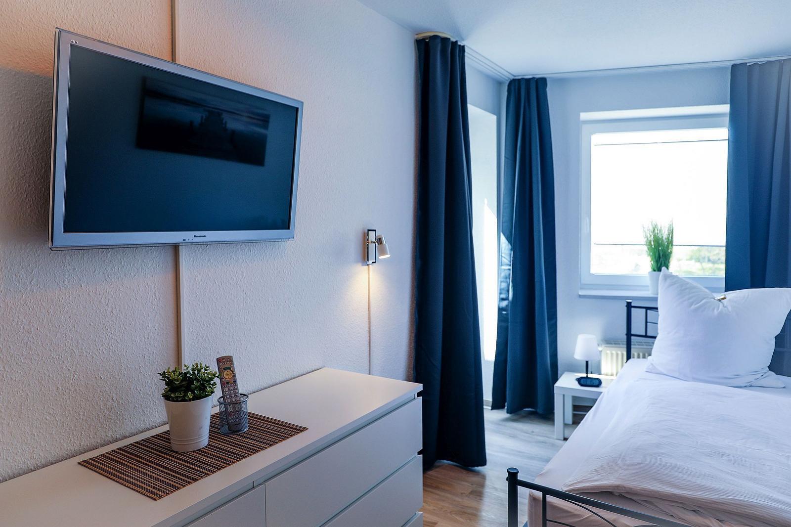 Schlafzimmer mit Bett, TV und Fenster mit Vorhängen.
