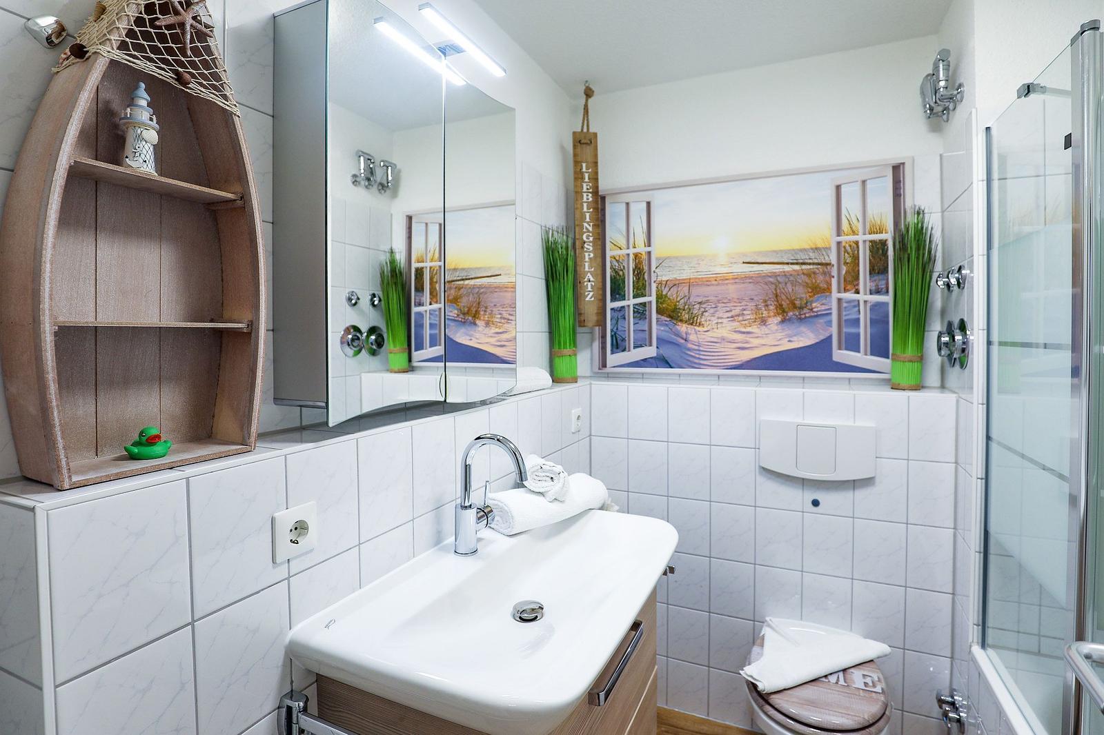 Badezimmer mit Dusche, Waschbecken und Wandbild mit Strandmotiv.