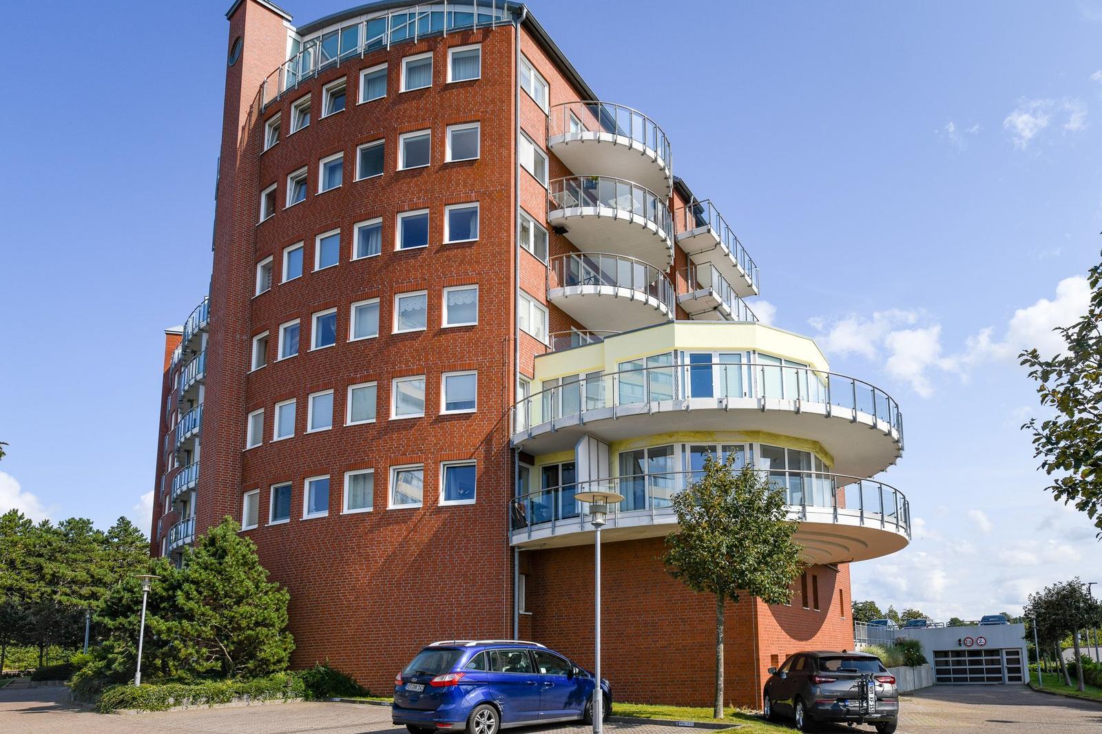 Hochhaus mit Balkonen und Parkplätzen unter blauem Himmel
