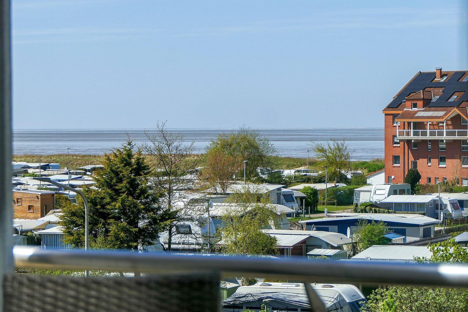 Blick vom Balkon auf Strand, Wohnmobile und ein rotes Gebäude.