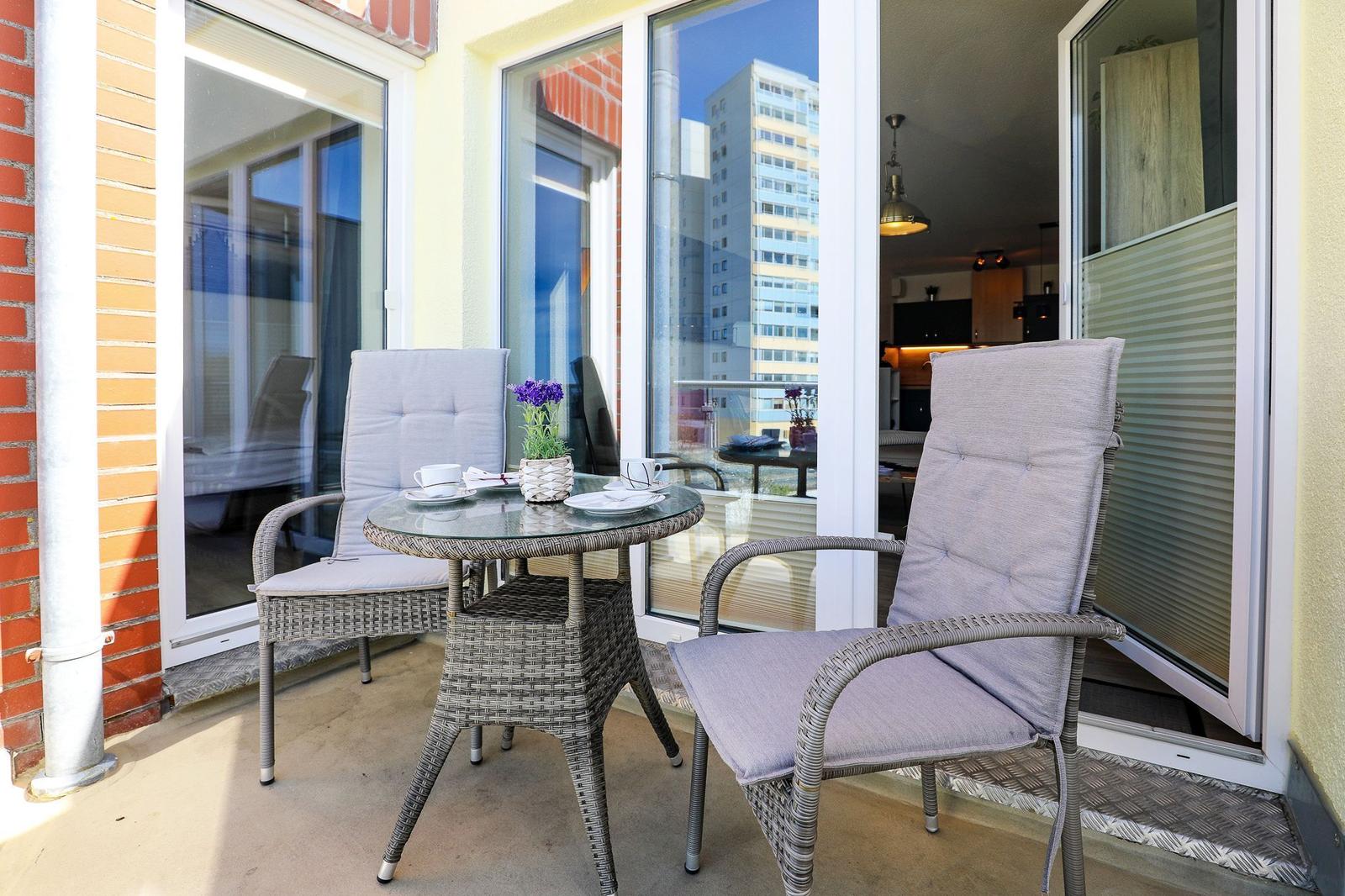 Terrasse mit zwei Stühlen und Tisch. Blick in Wohnbereich. Hochhaus im Hintergrund.