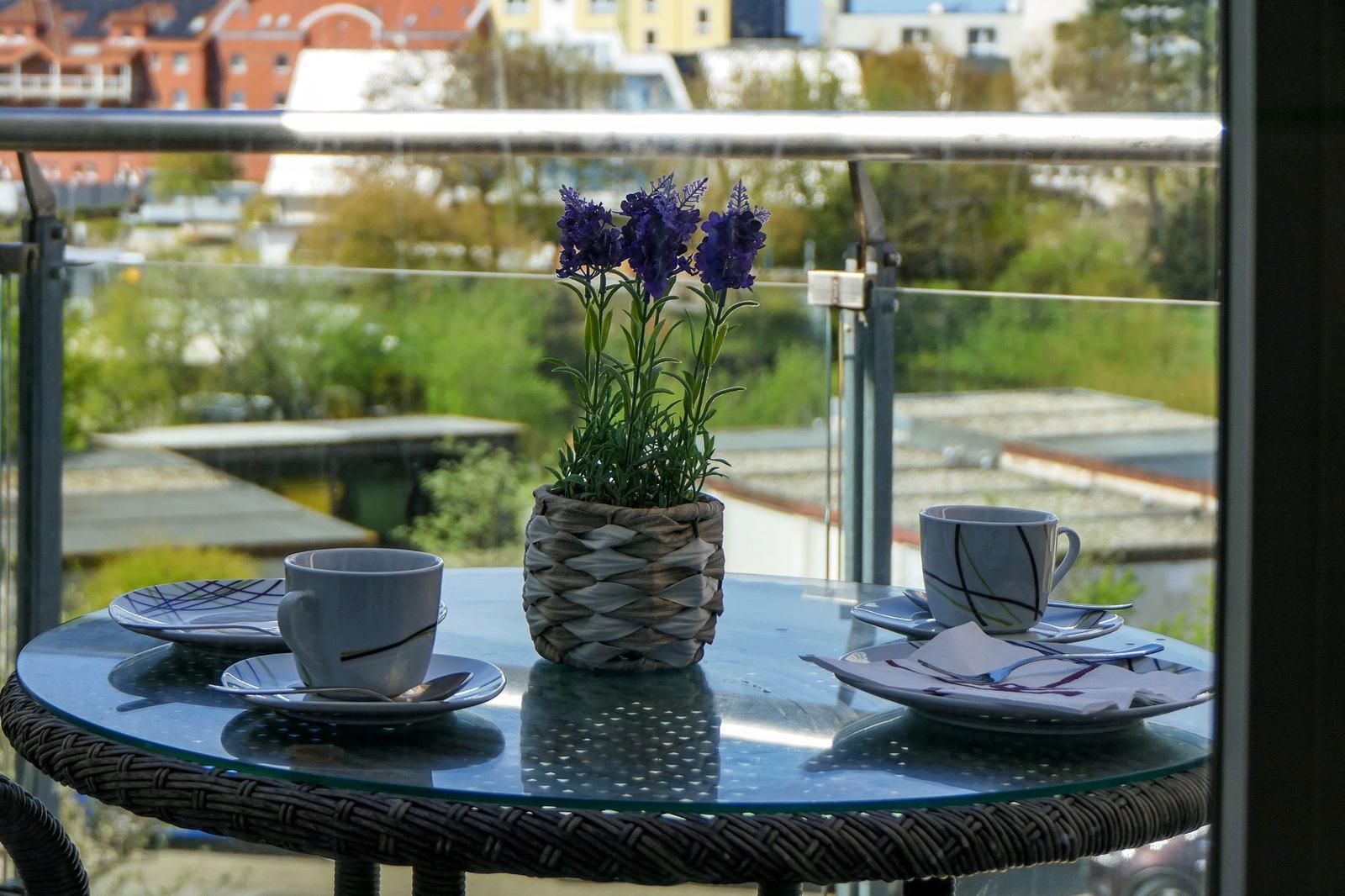 Auf der Terrasse steht ein Tisch mit zwei Tassen, Tellern und einer Pflanze in einem Korb.