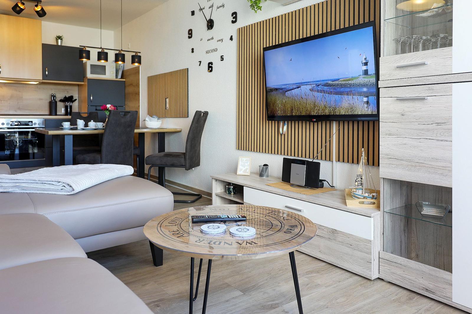 Wohnbereich mit TV, Esstisch und Küchenzeile. Holzakzentwand und moderner Couchtisch.