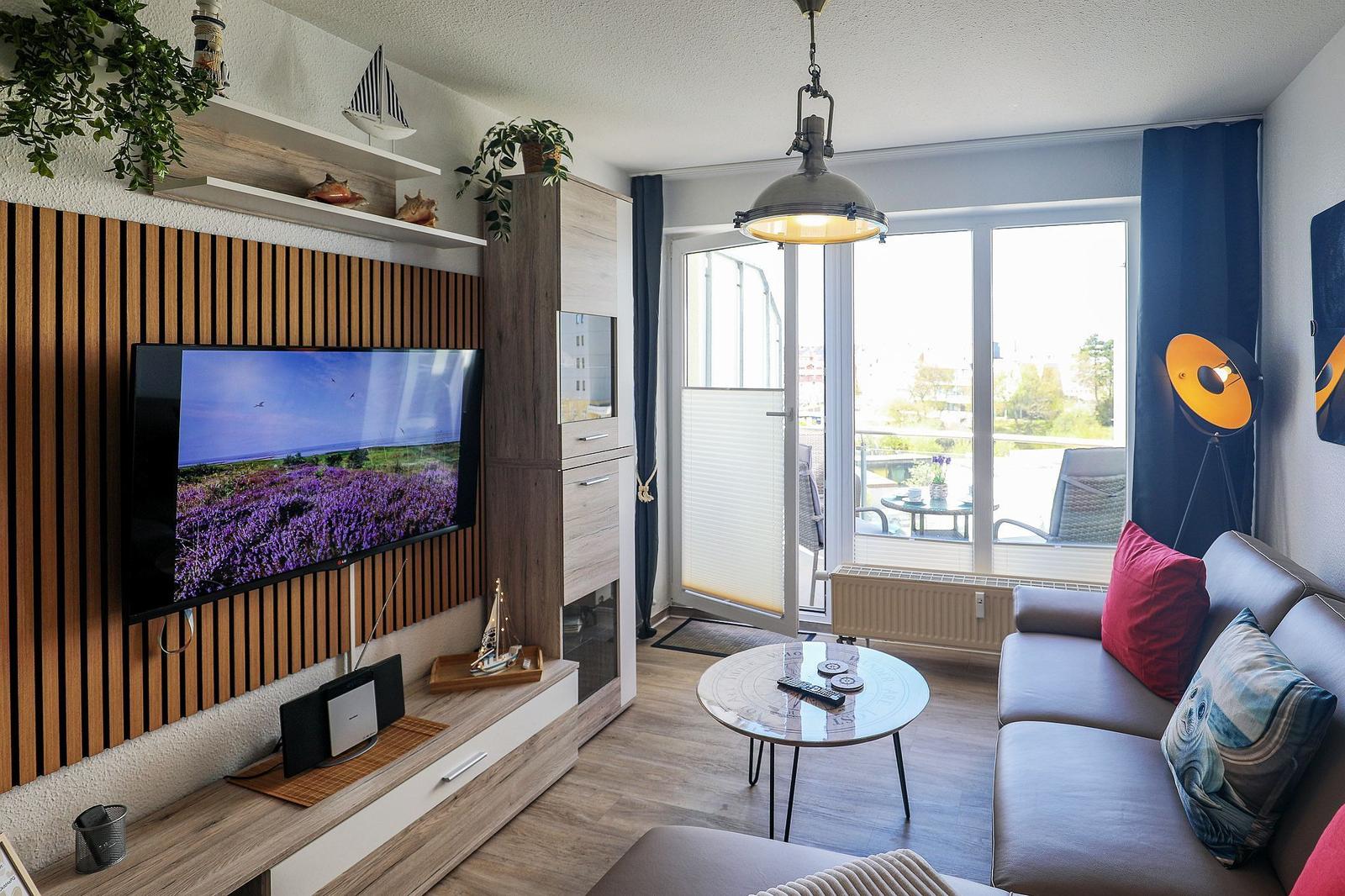 Wohnzimmer mit Sofa, TV und Balkonansicht