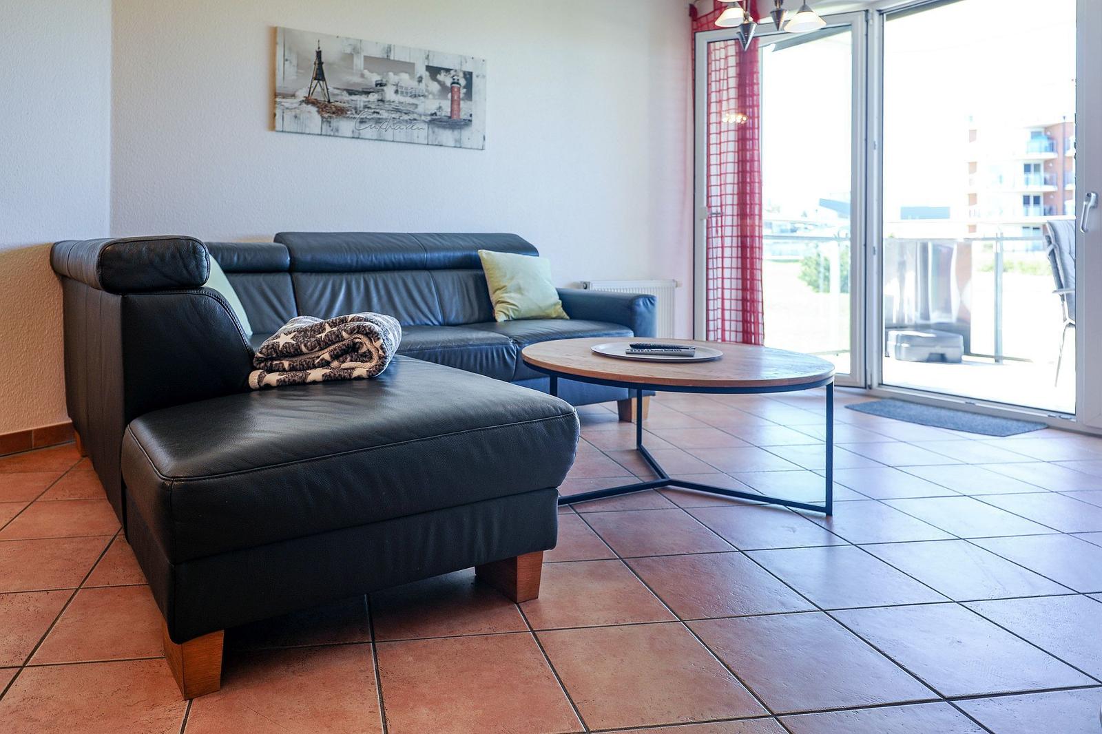 Schwarzes Ledersofa mit Kissen und Decke, runder Tisch, Terrasse mit Blick.