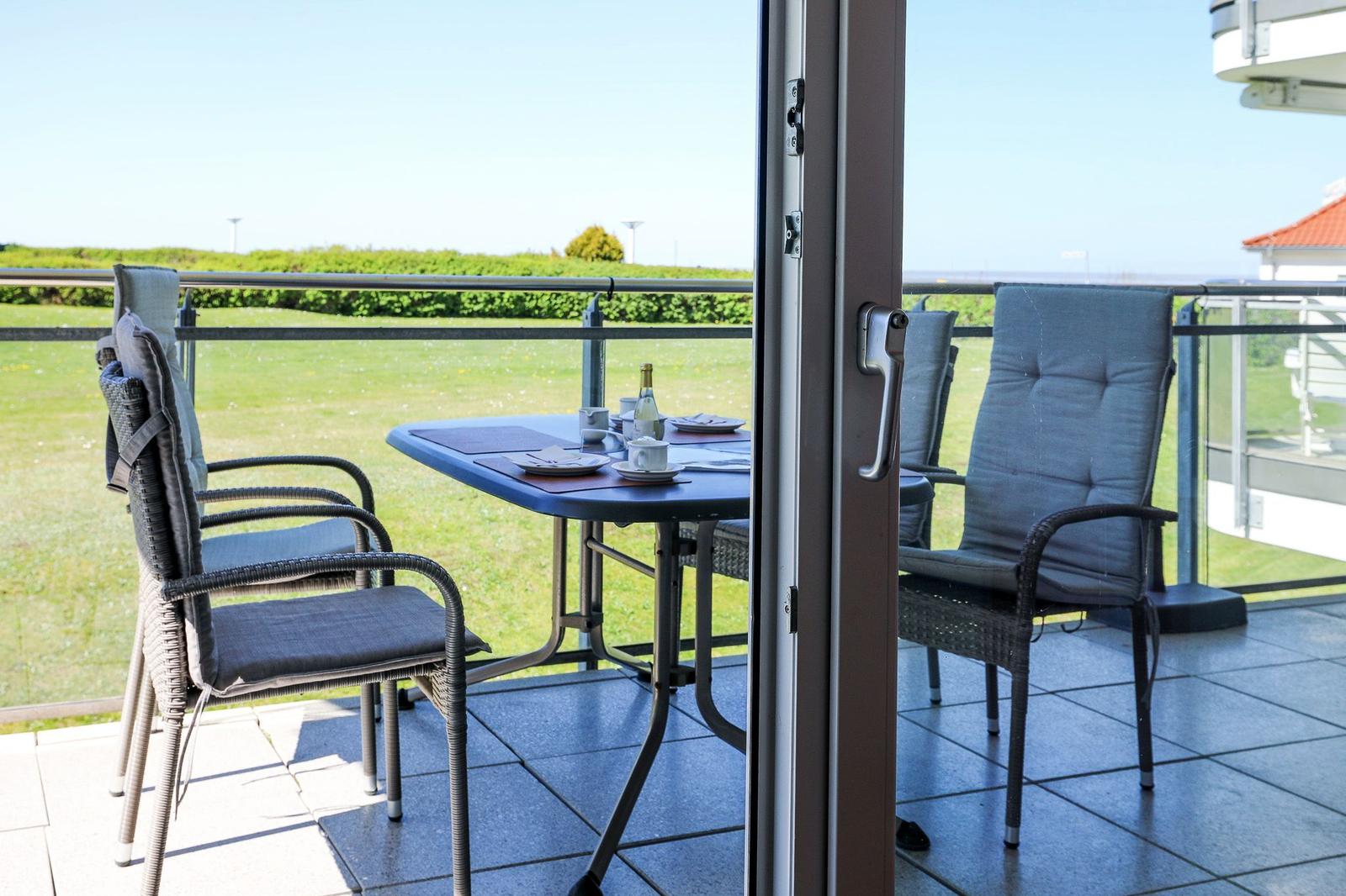 Terrasse mit Tisch und Stühlen, Blick auf Grünfläche und Horizont.