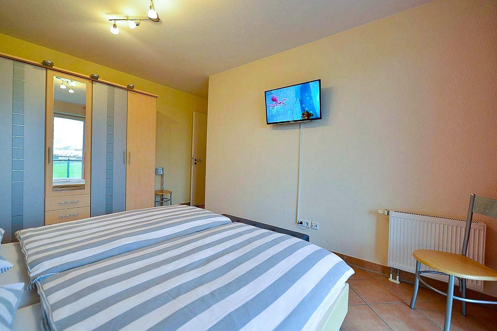 Schlafzimmer mit Bett, Kleiderschrank, Fernseher und Stuhl.