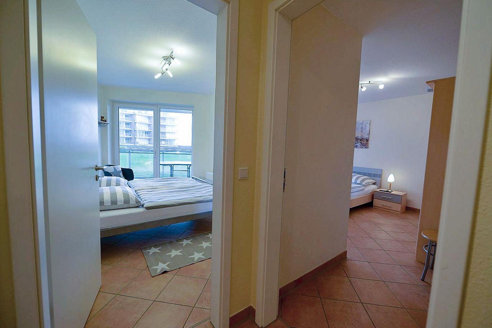 Zwei Schlafzimmer mit Betten, Fenstern und Lampen. Fliesenboden und Türöffnungen.