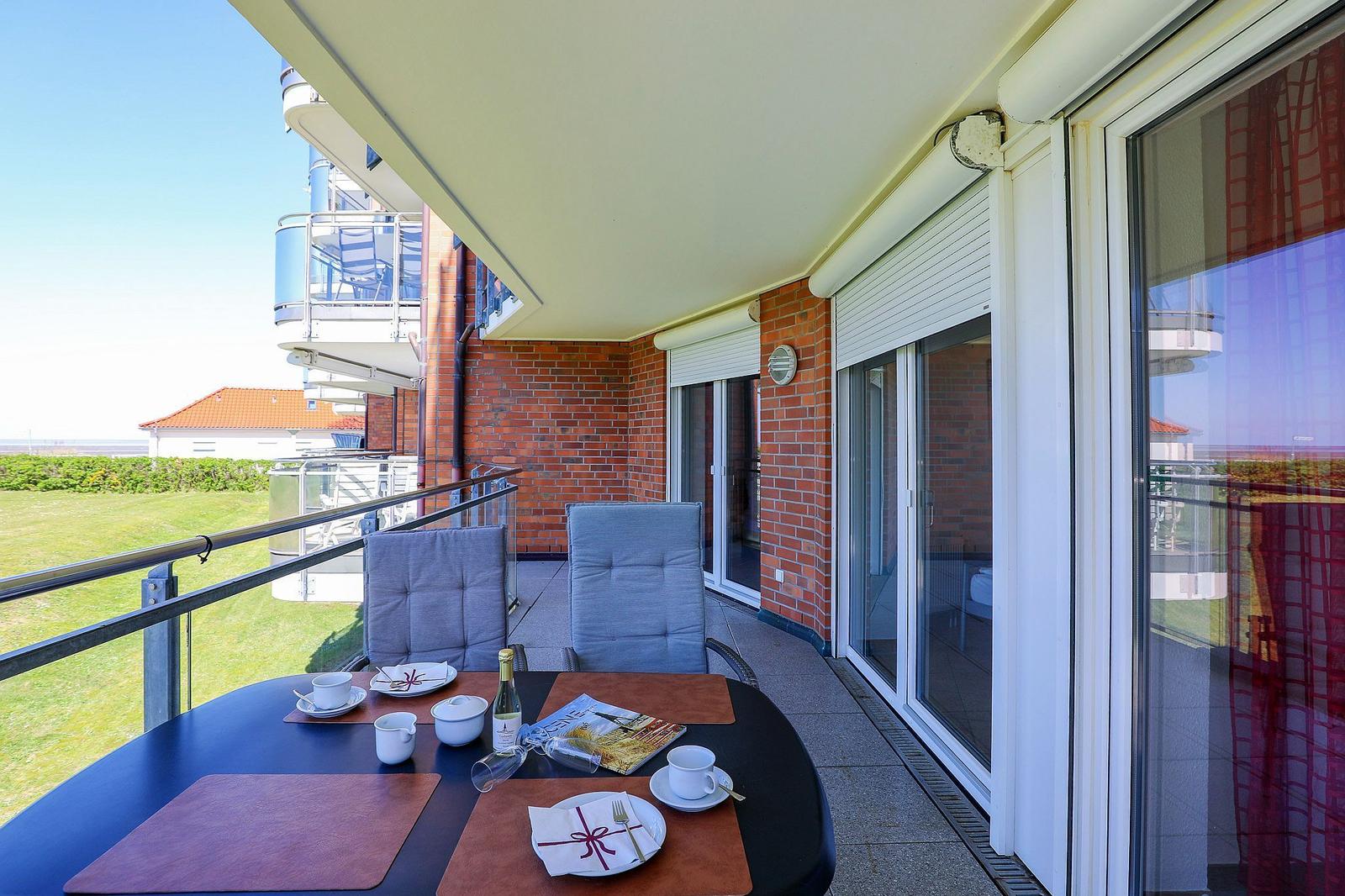 Terrasse mit Tisch, Stühlen und Blick auf Grünfläche und Gebäude.