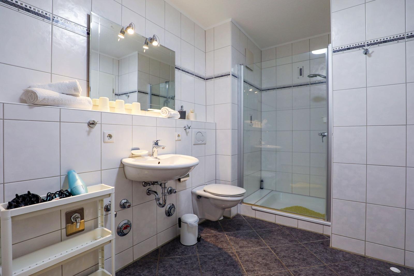 Badezimmer mit Dusche, Waschbecken und Toilette. Fliesenwand und dunkler Boden.