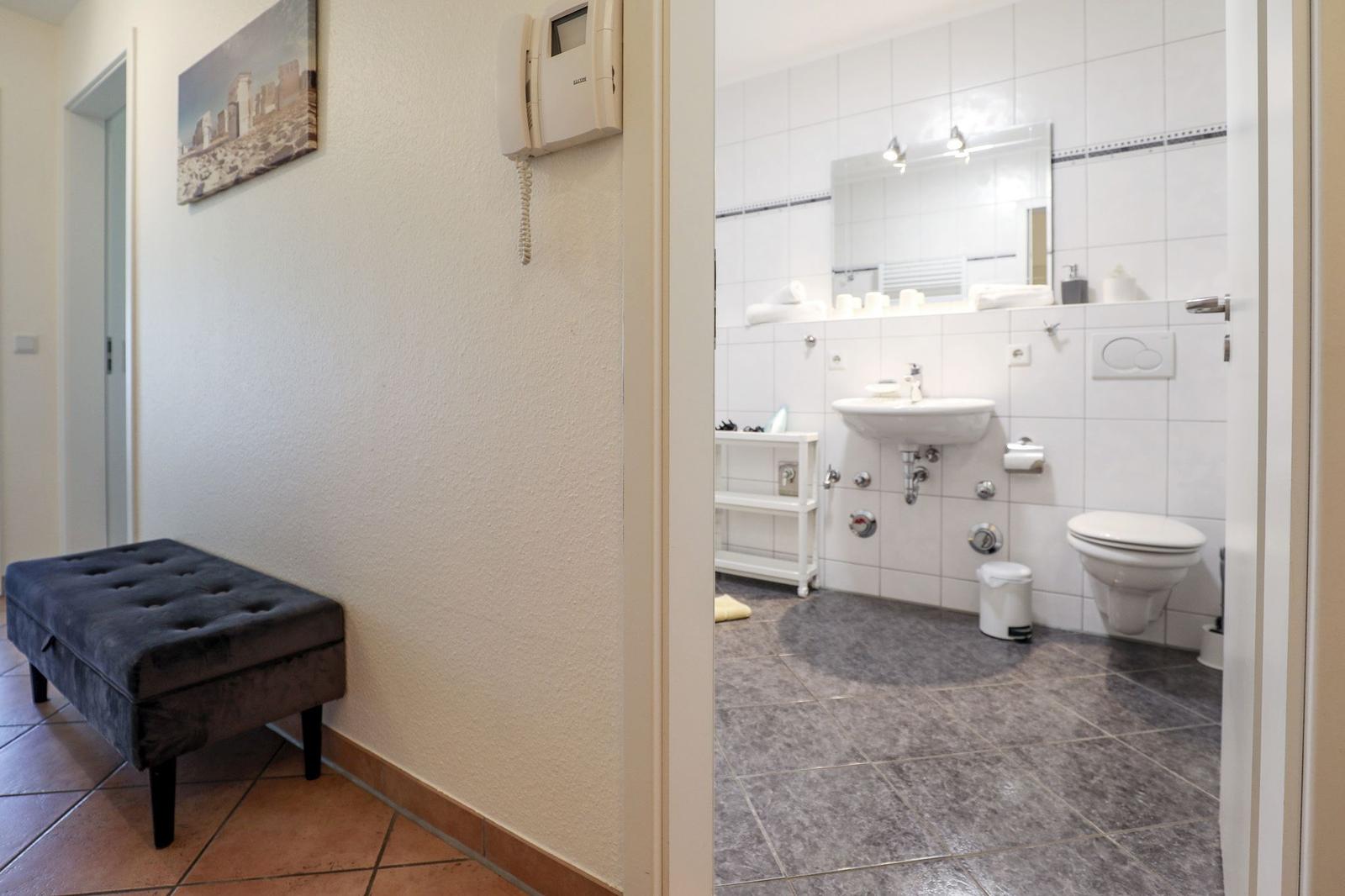 Flur mit Sitzbank und Blick in das Badezimmer mit Waschbecken und WC.