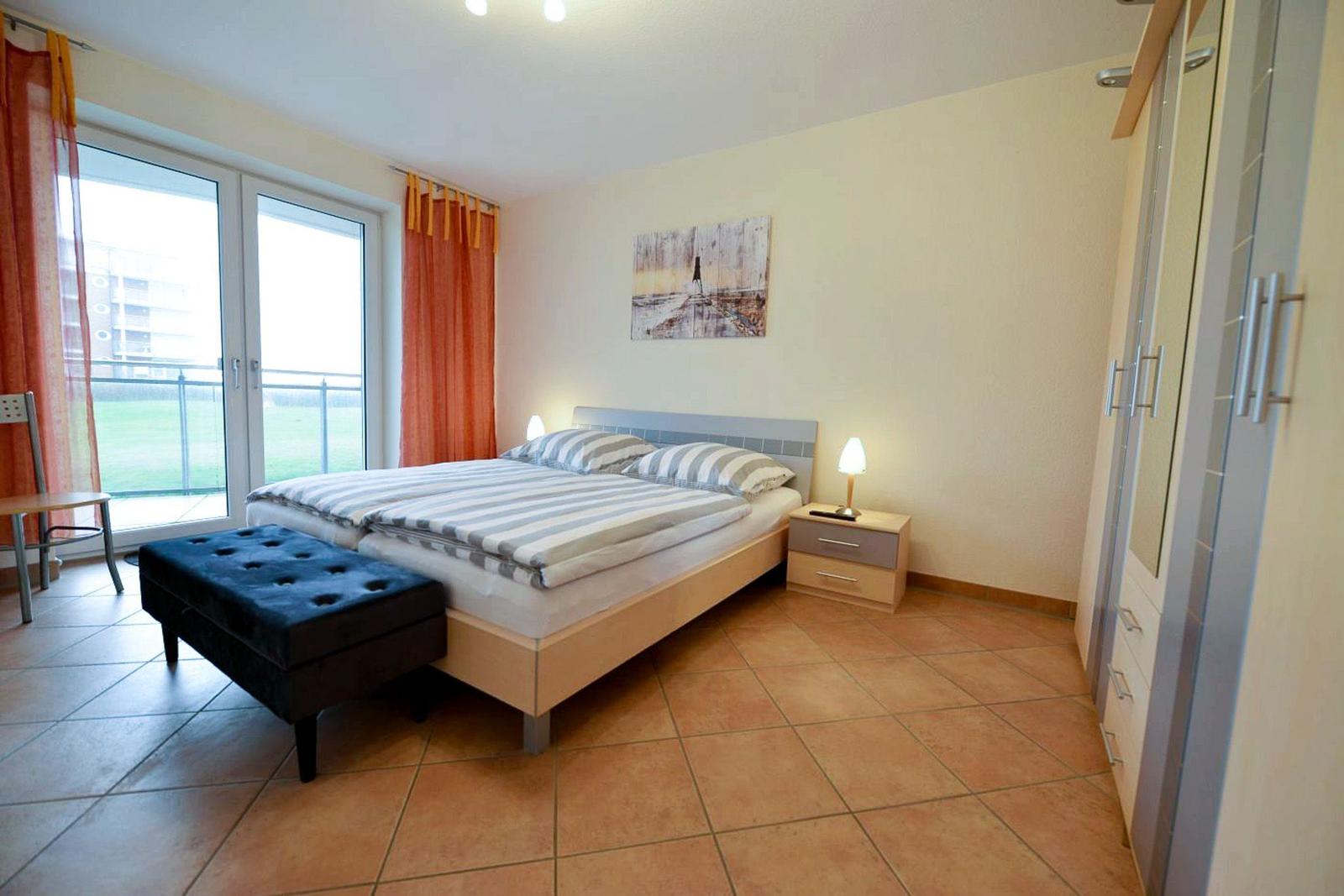Schlafzimmer mit Doppelbett, Schreibtisch, Garderobe und Blick auf Balkon.