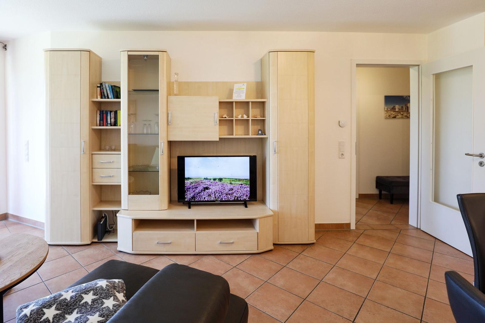 Wohnzimmer mit TV, Holzmöbel und Terrakottaboden. Türen führen in angrenzende Räume.