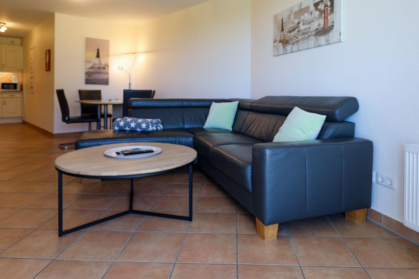 Ein Wohnzimmer mit einem schwarzen Sofa, einem runden Tisch und einer Küchenzeile im Hintergrund.