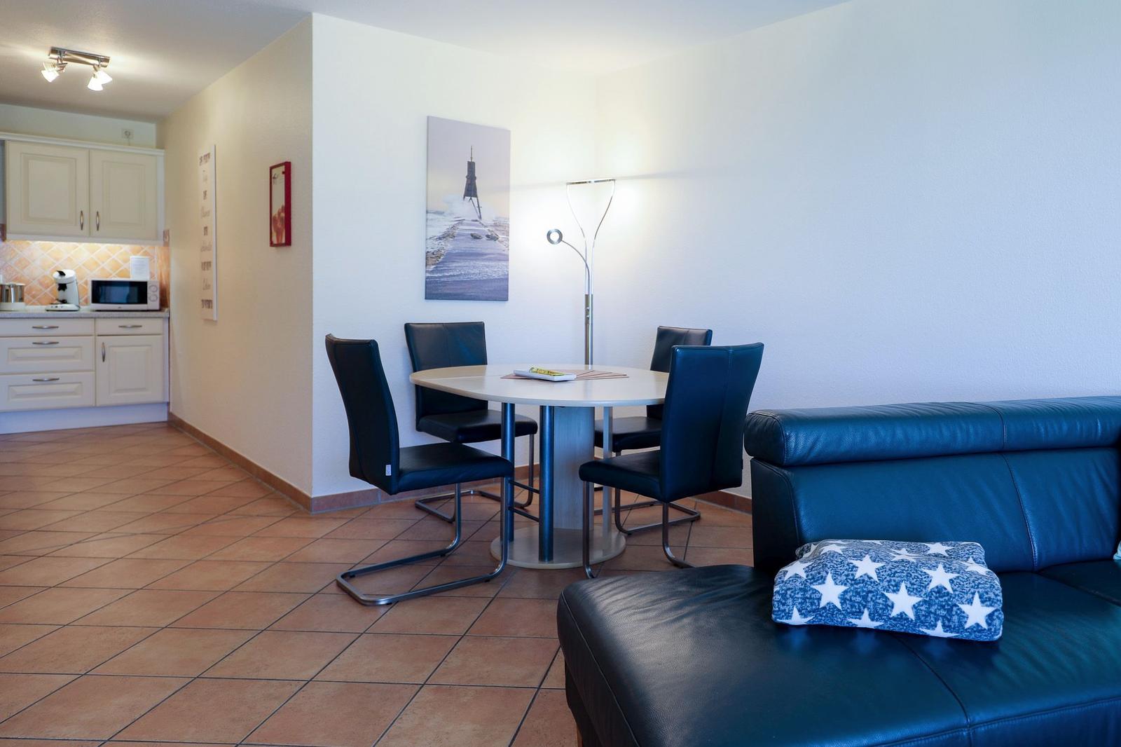 Wohn- und Essbereich mit Sofa, Tisch und Stühlen. Küche im Hintergrund.